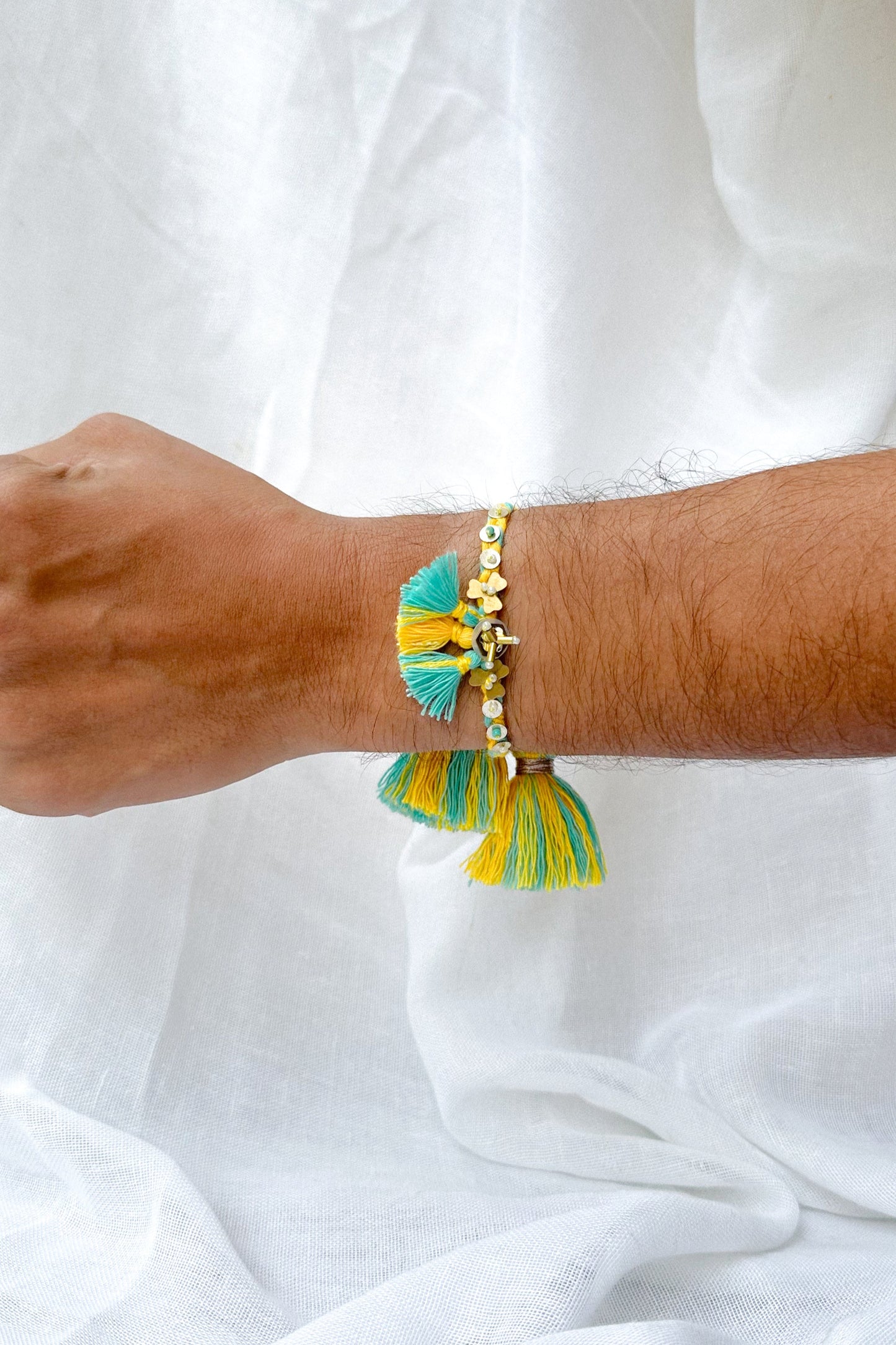 Bracelet with yellow and green tassels on a wrist against a white background