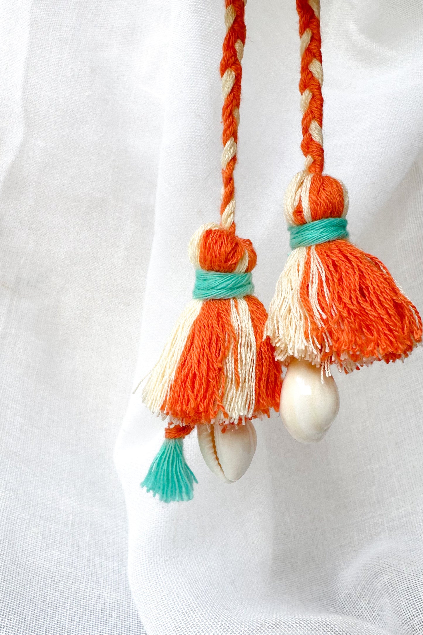 Decorative tassels with orange, white, and turquoise strings on a white background
