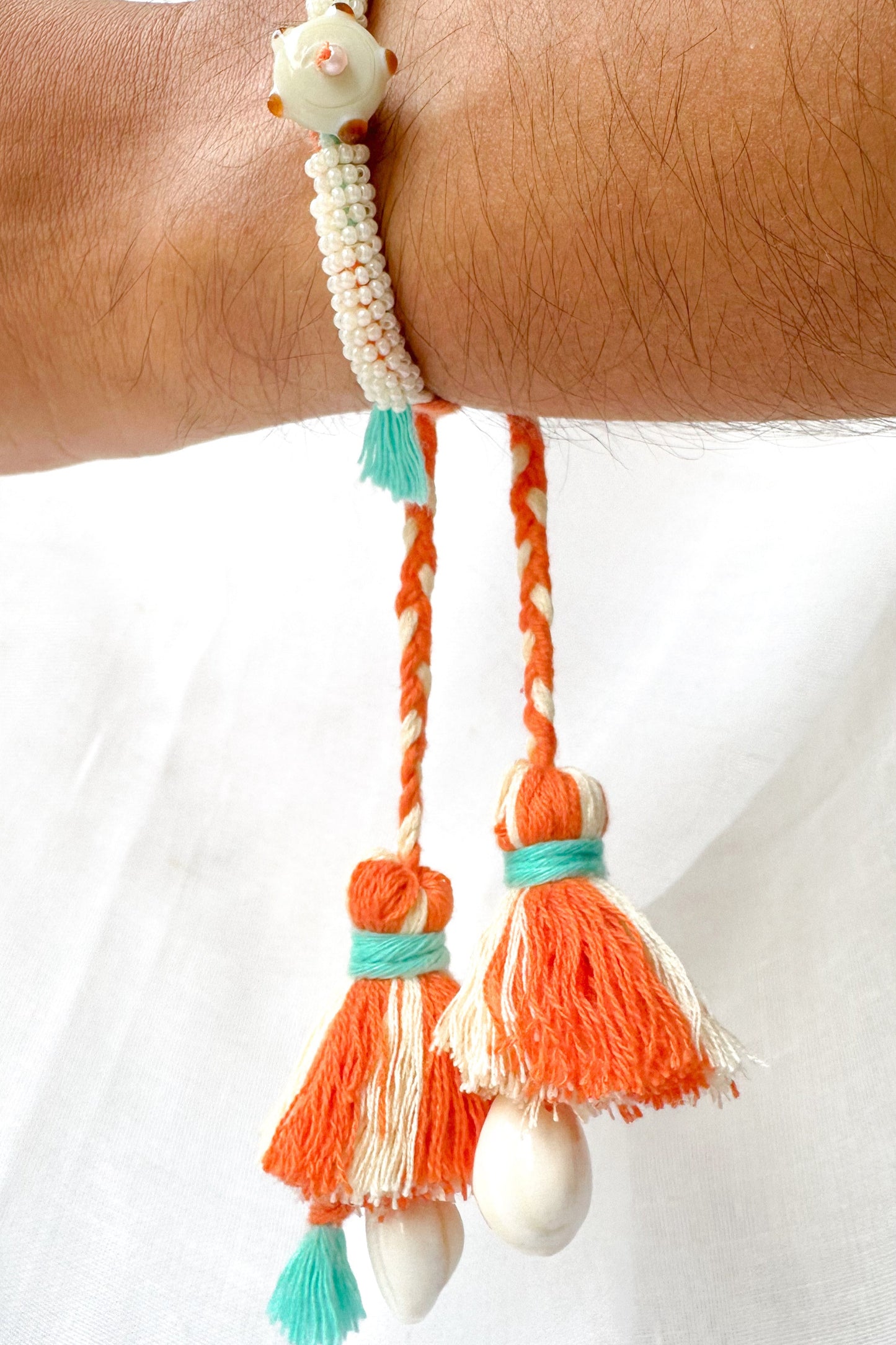 Bracelet with orange tassels and white beads on a wrist against a white background