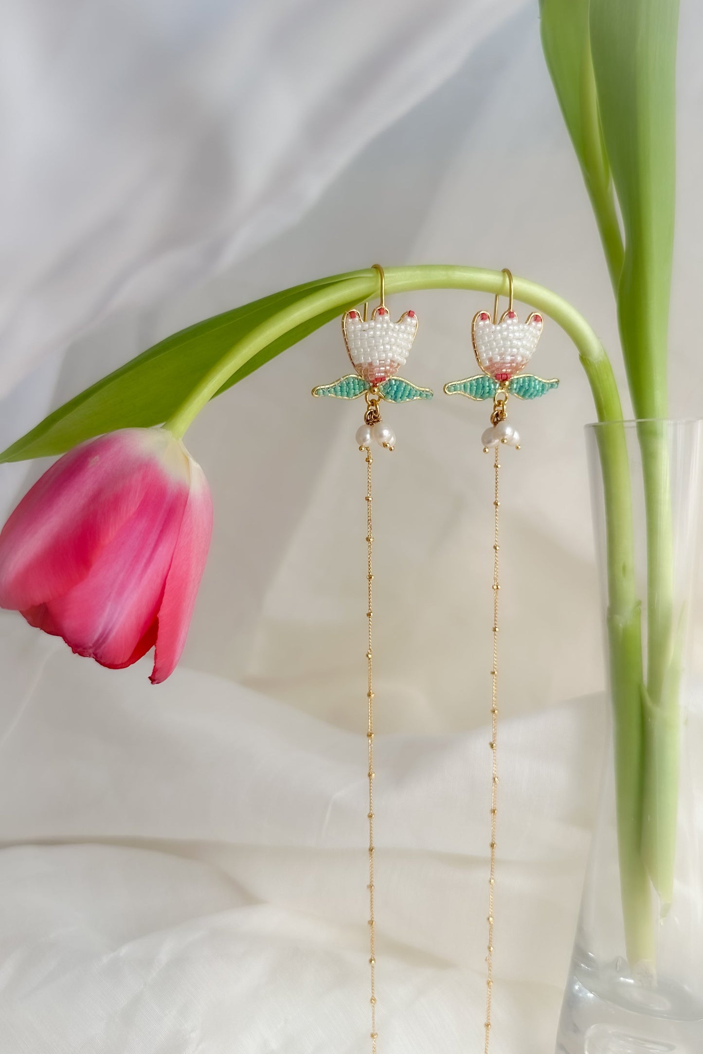 Gold earrings with green accents on a white background with pink tulips
