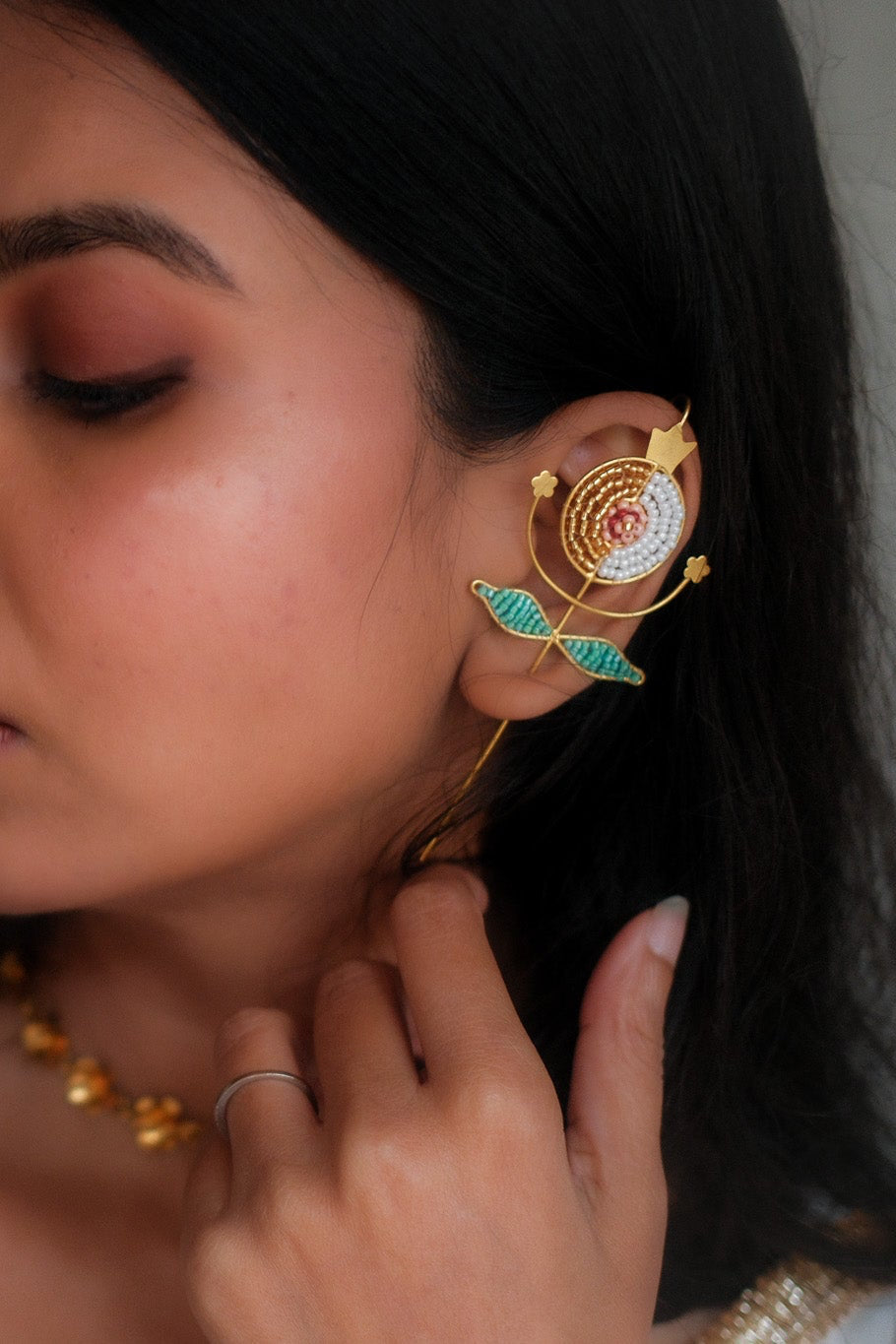 Woman wearing gold ear cuffs with pomegranate motif with a gray background