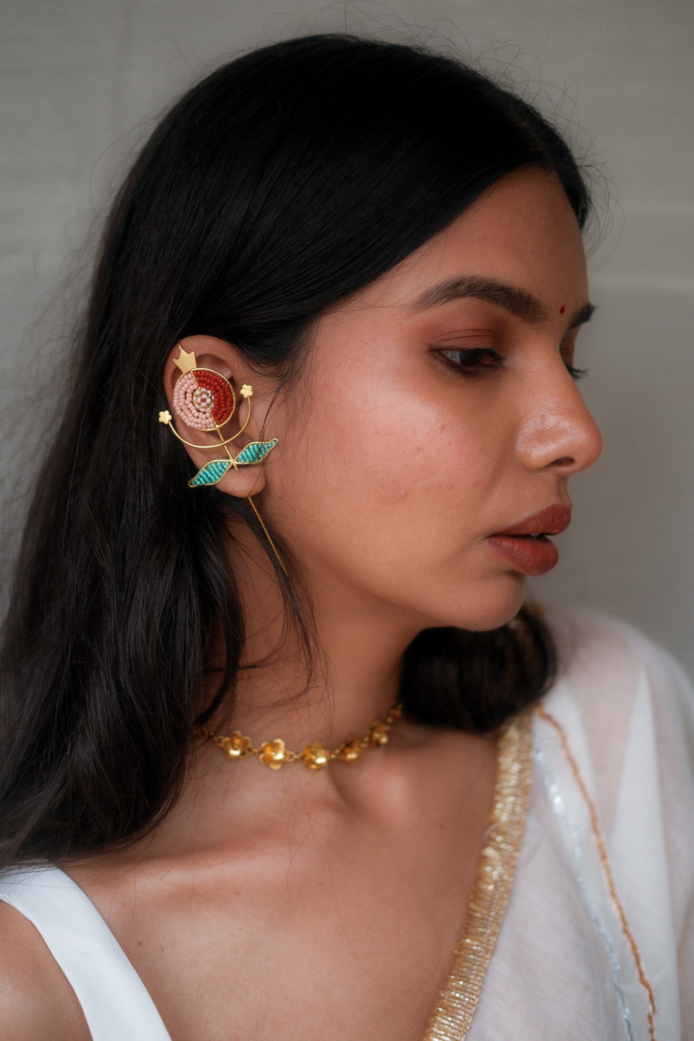 Woman wearing intricate earrings with pomegranate motif  against a neutral background