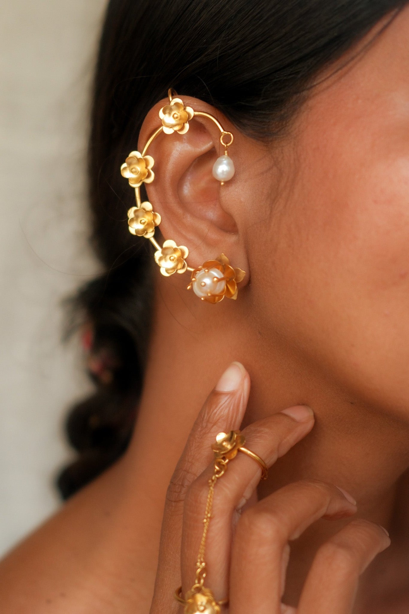 Close-up of a person wearing gold floral earrings with pearl accents.