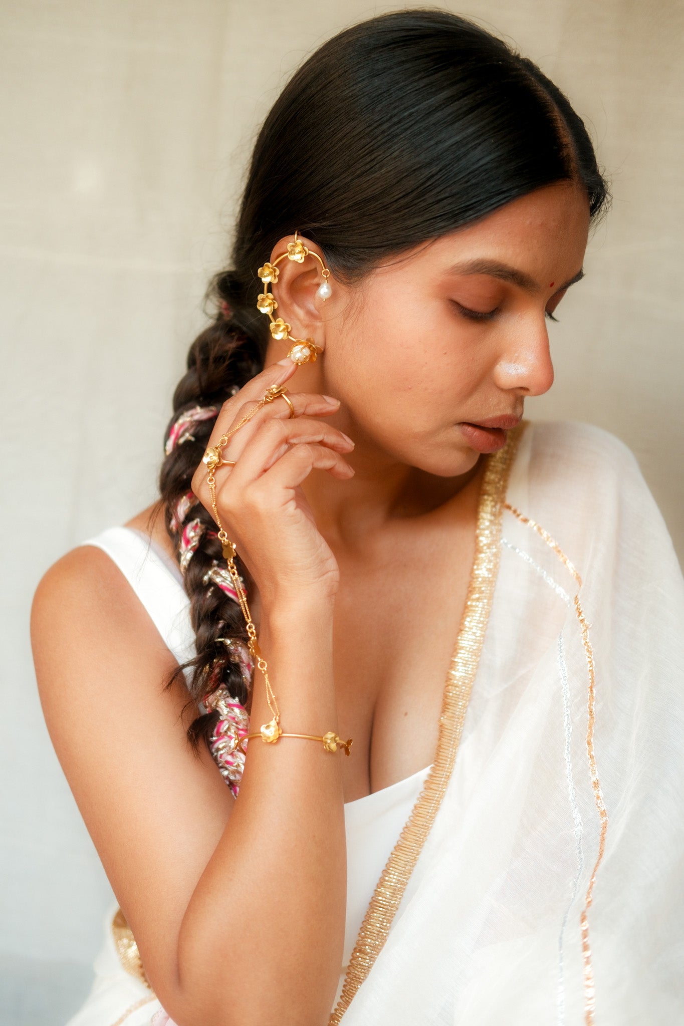 Woman wearing gold earrings and a bracelet, looking down.