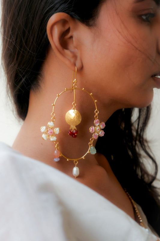 Close-up of a person wearing gold hoop earrings with colorful beads & Pomegranate Motif.