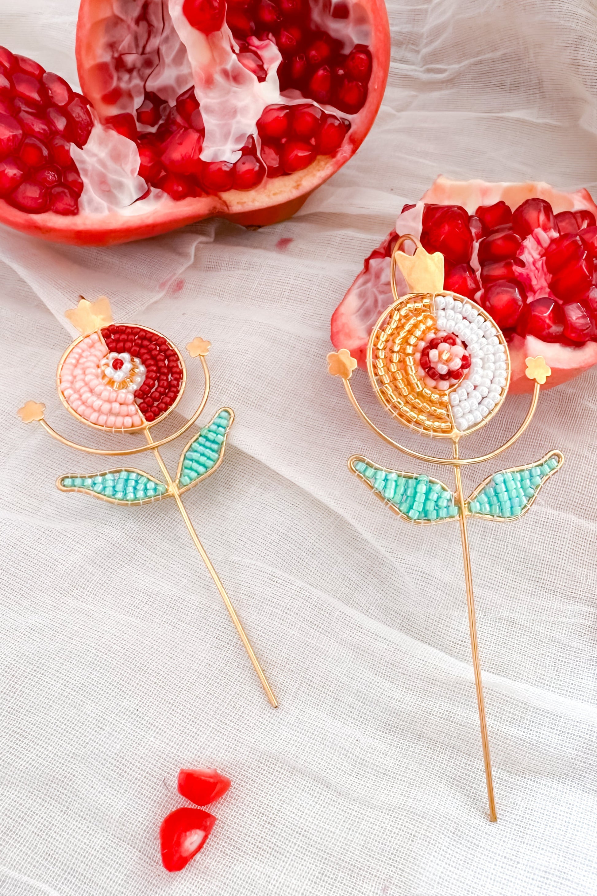 Two decorative pomegranate-shaped ear cuffs on a white fabric background with pomegranate pieces.