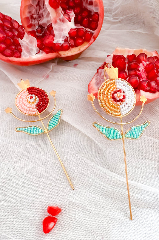 Two decorative pomegranate-shaped ear cuffs on a white fabric background with pomegranate pieces.