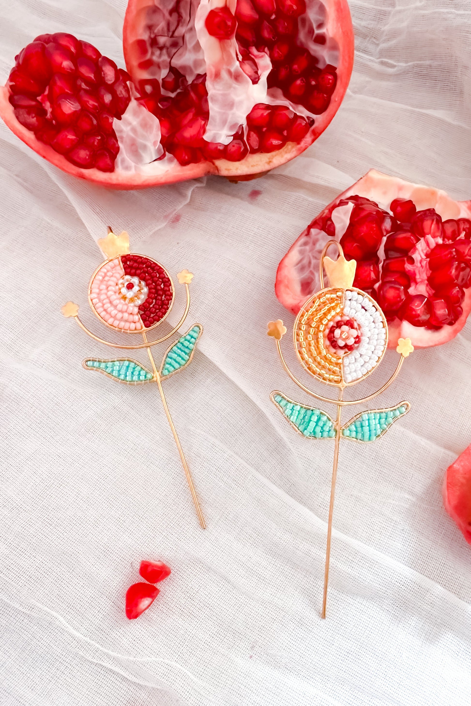 Pomegranate cut open with seeds visible, accompanied by decorative Ear Cuffs on a light fabric background.