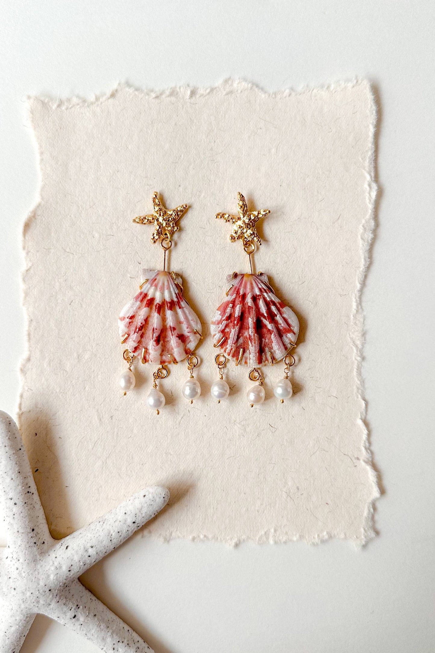 Pair of shell-shaped earrings with gold accents on a textured white surface.