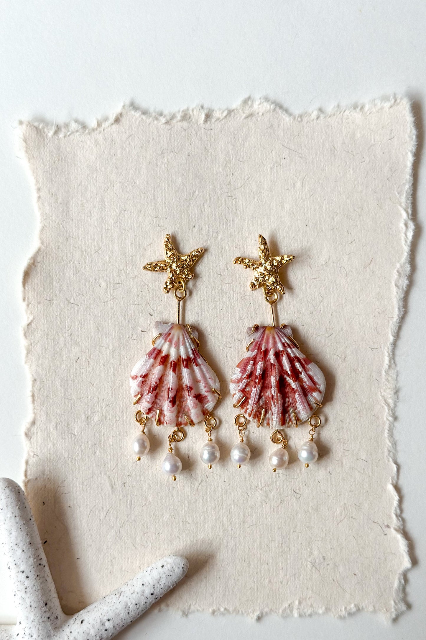Shell and pearl earrings on a textured white surface with a light background