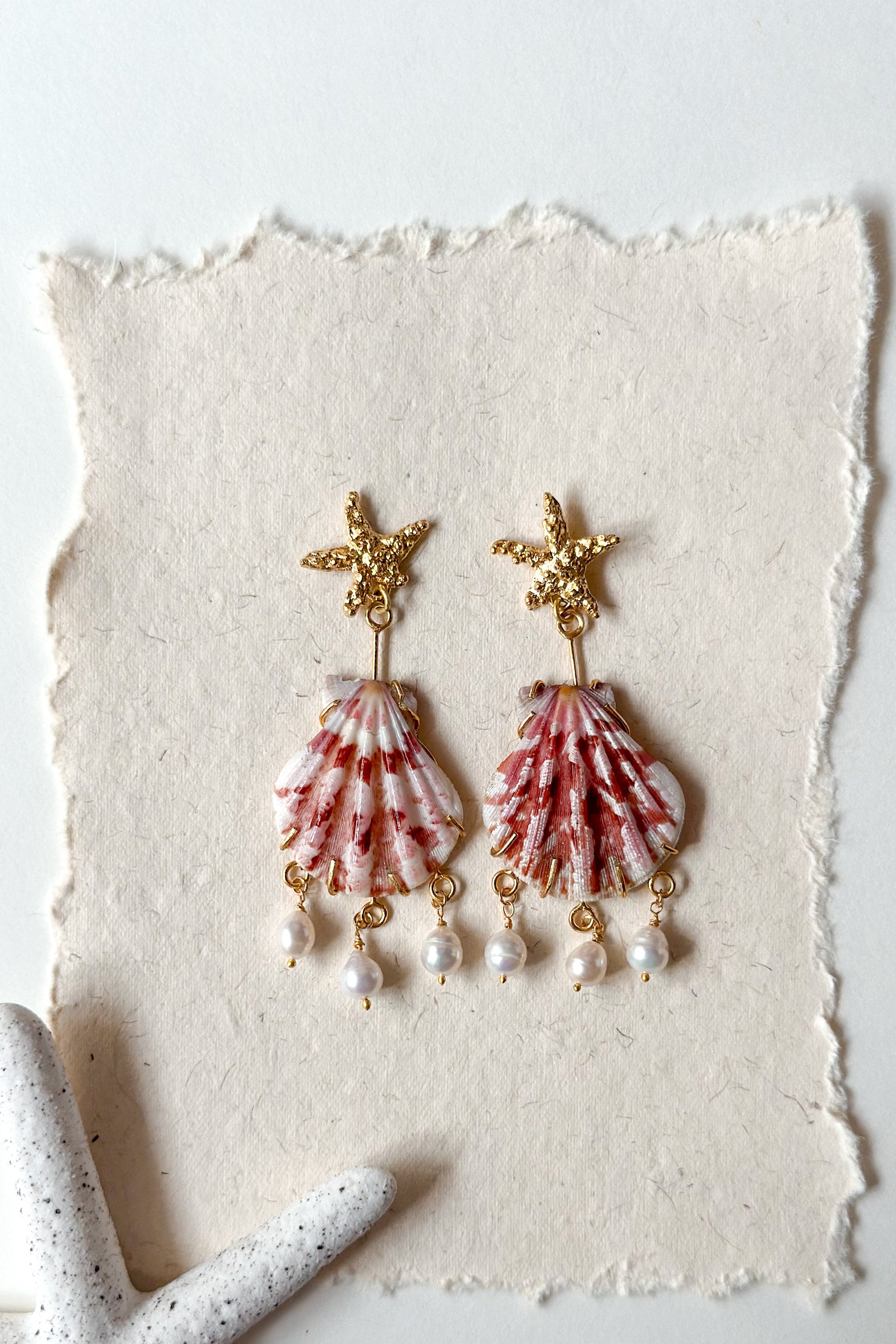 Shell and pearl earrings on a textured white surface with a light background