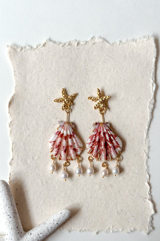 Shell and pearl earrings on a textured white surface with a light background