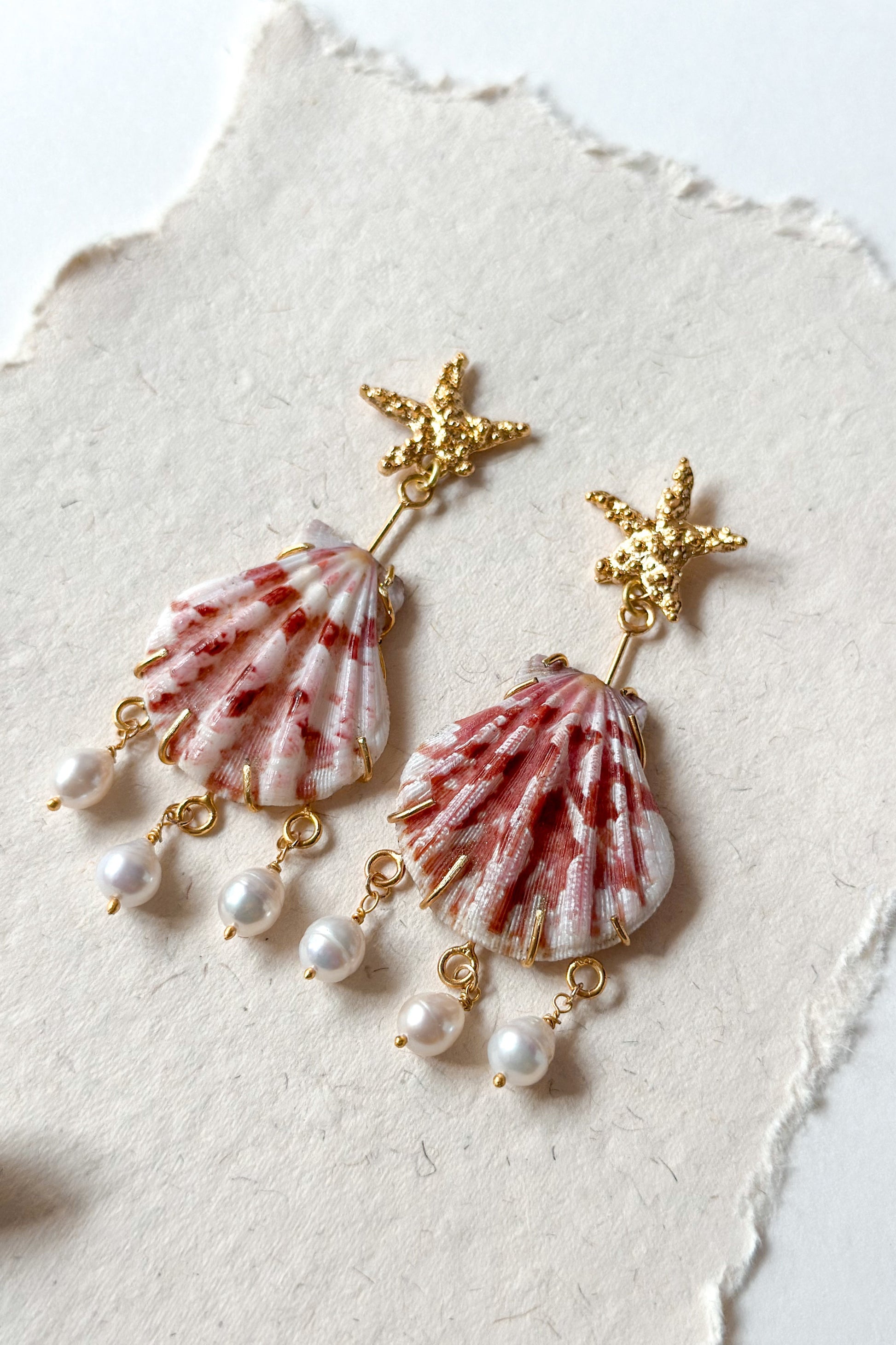 Shell and pearl earrings on a textured white surface