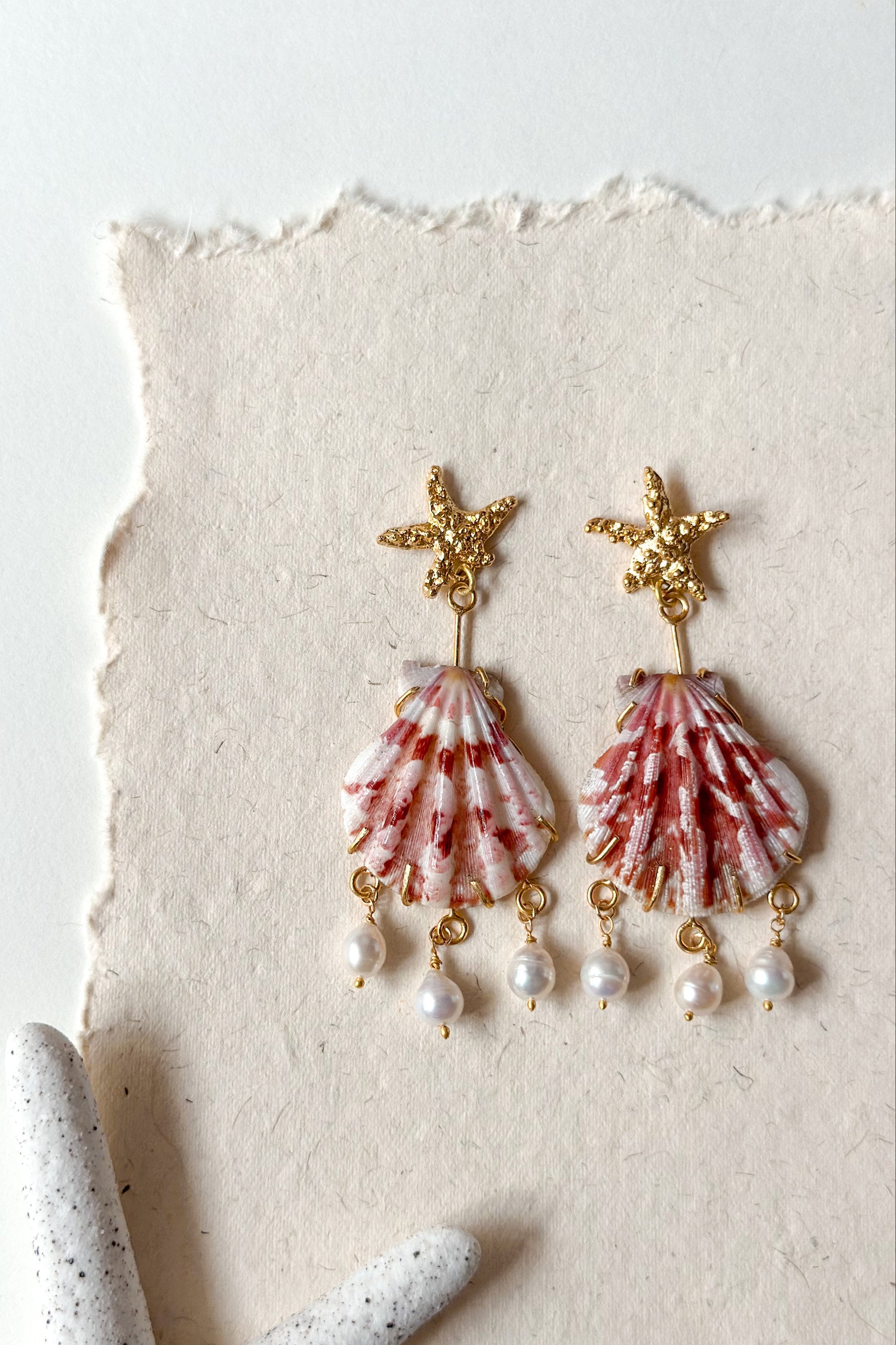 Shell and pearl earrings with starfish designs on a textured white background