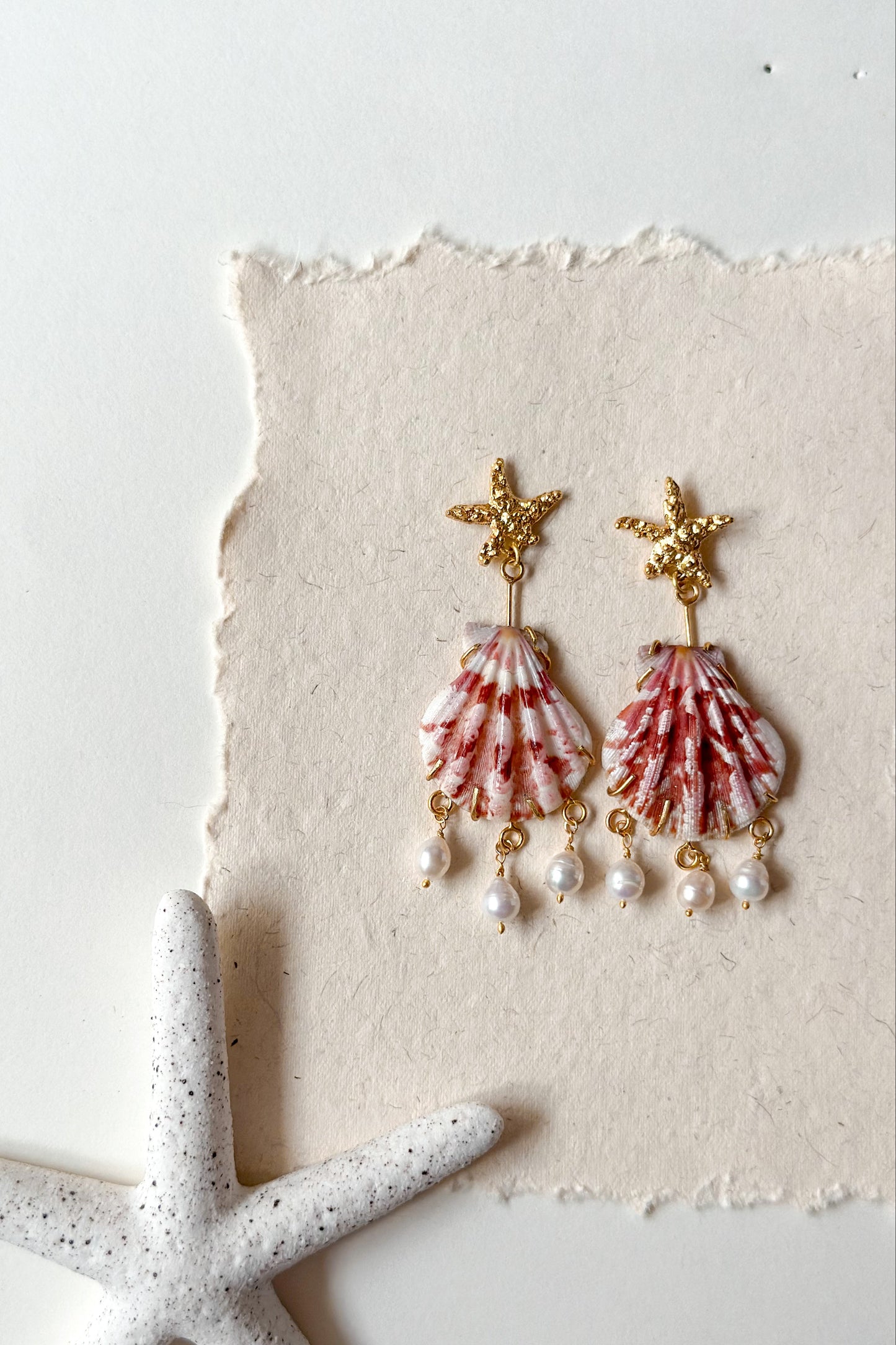 Shell and pearl earrings on a textured white surface with a starfish.