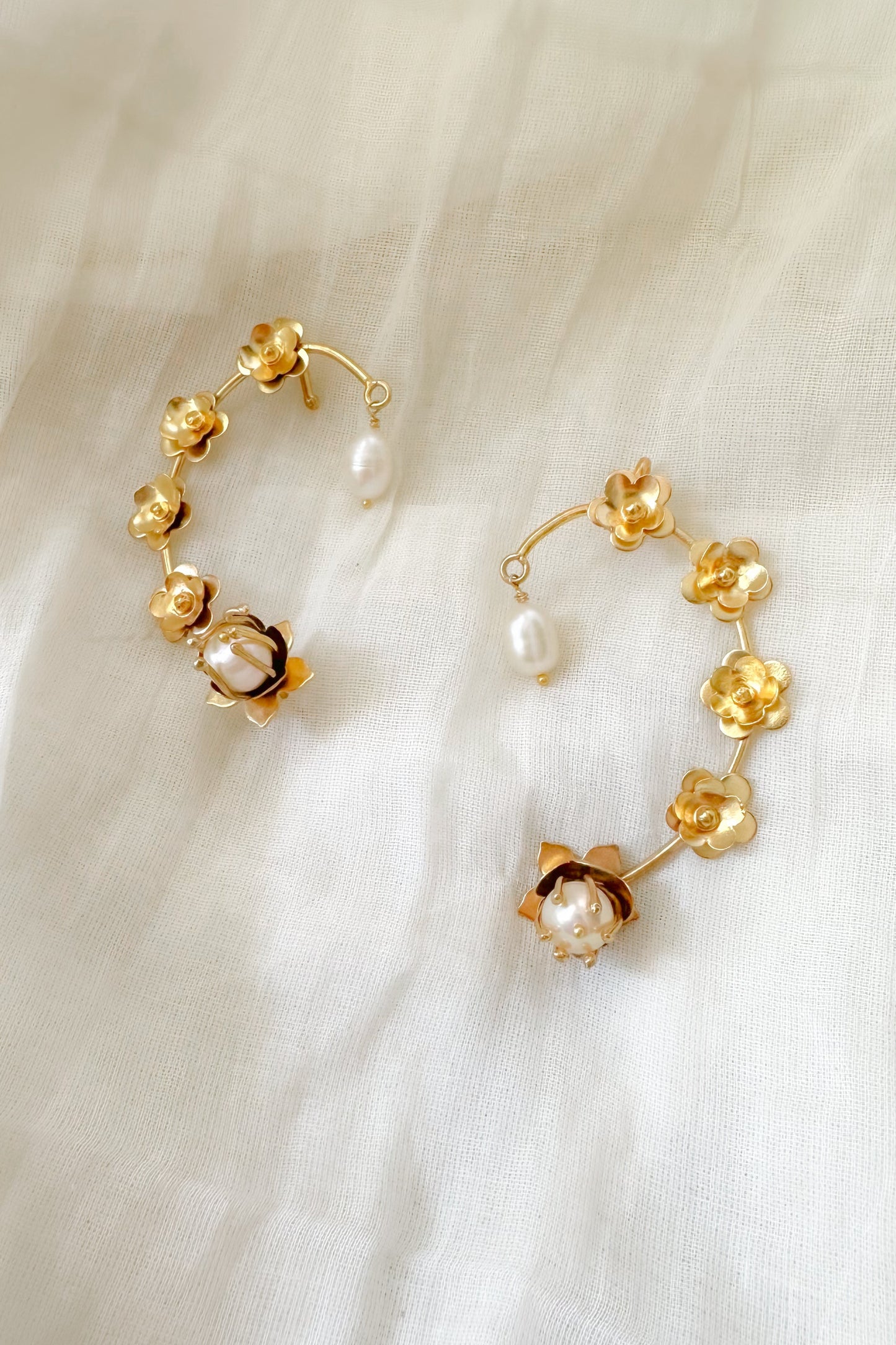 Gold Ear cuffs with pearl accents on a white fabric background