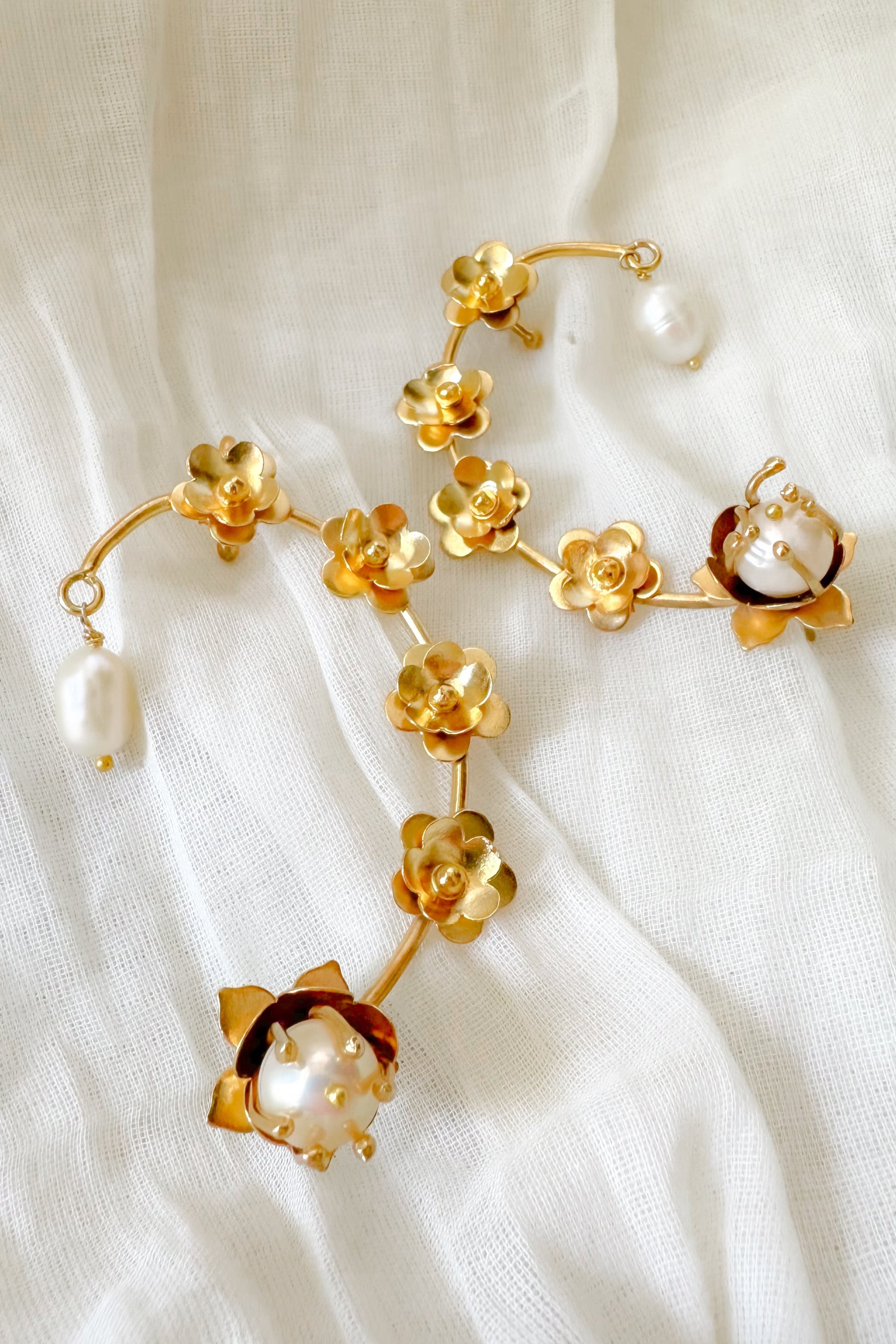 Gold floral earcuffs with pearl accents on a white fabric background