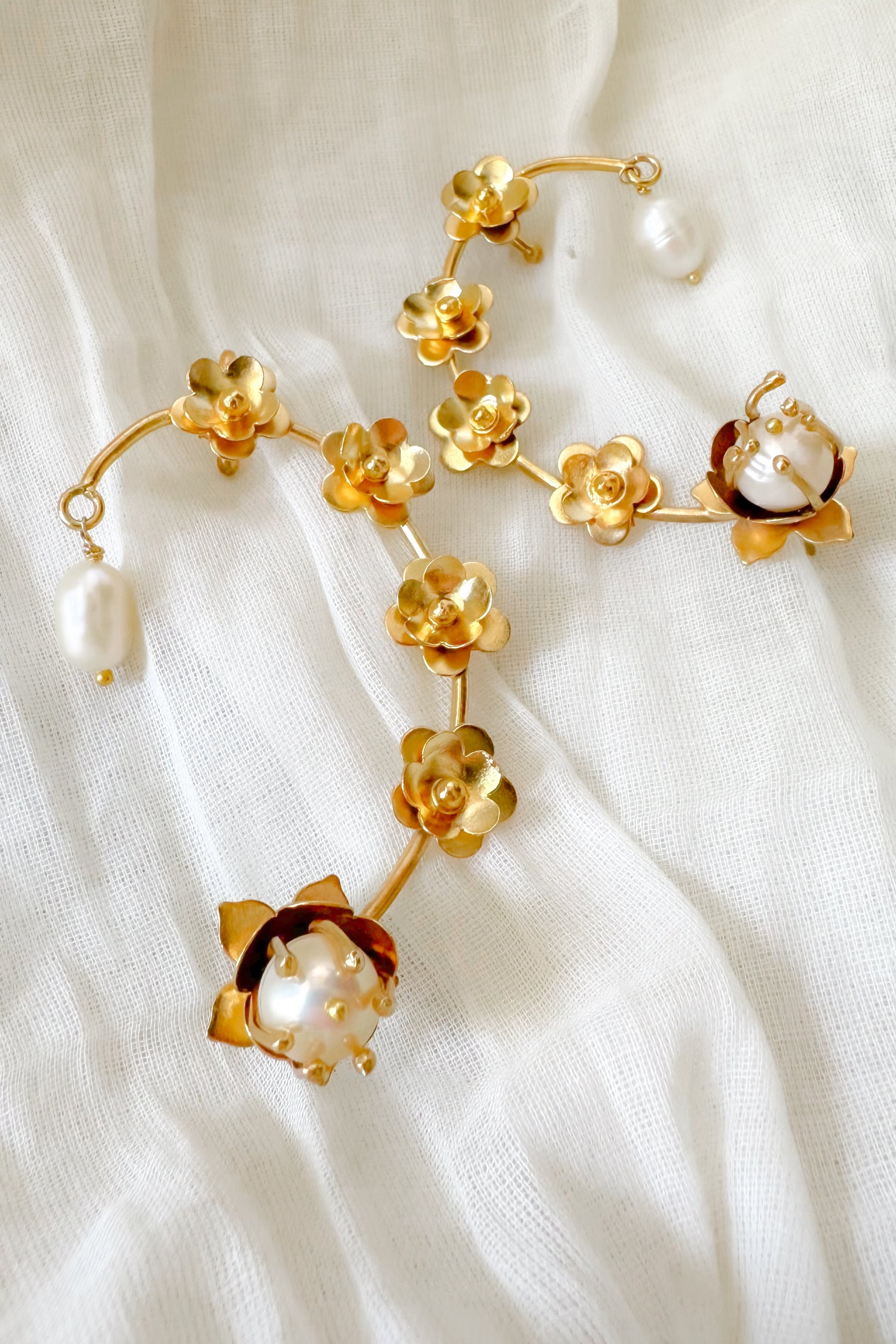 Gold floral earrings with pearl accents on a white fabric background