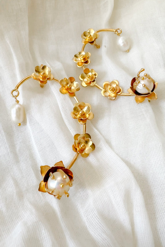 Gold floral earrings with pearl accents on a white fabric background