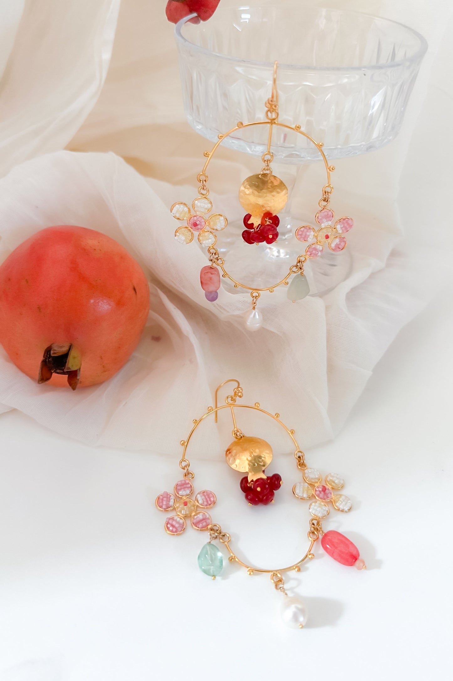 Decorative earrings with colorful beads and a pomegranate on a light fabric background