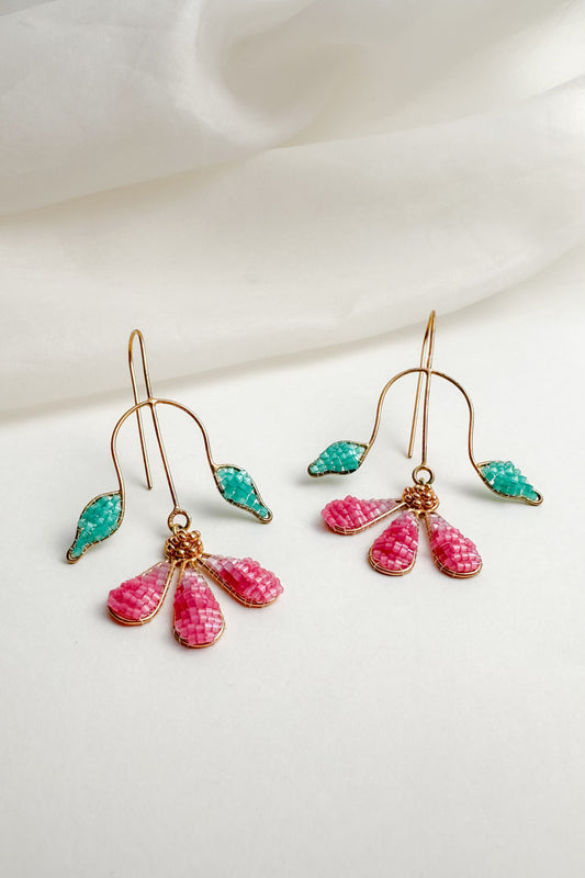 Pair of earrings with pink and green drops on a white fabric background