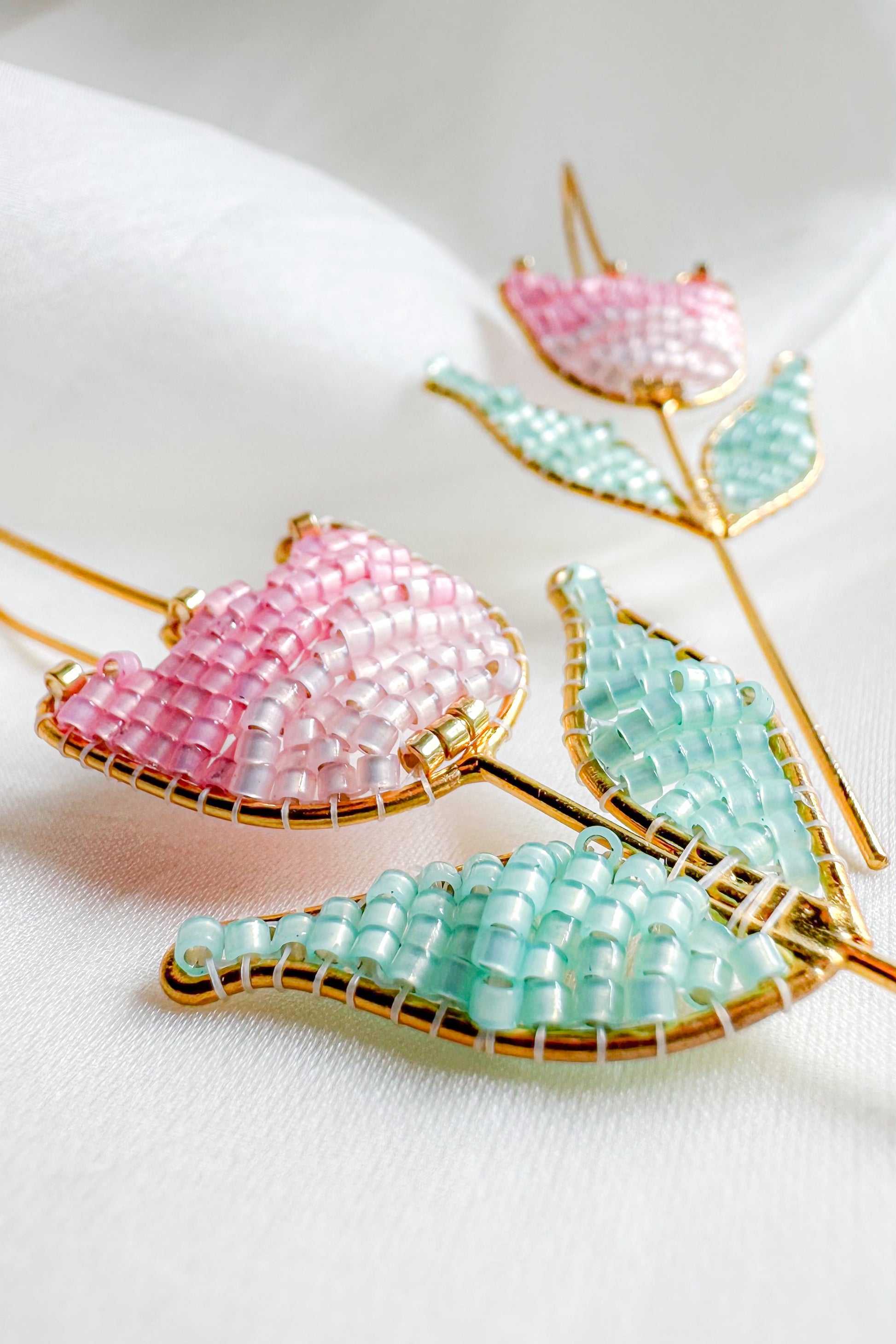 Beaded pink and green leaf-shaped earrings on a white background