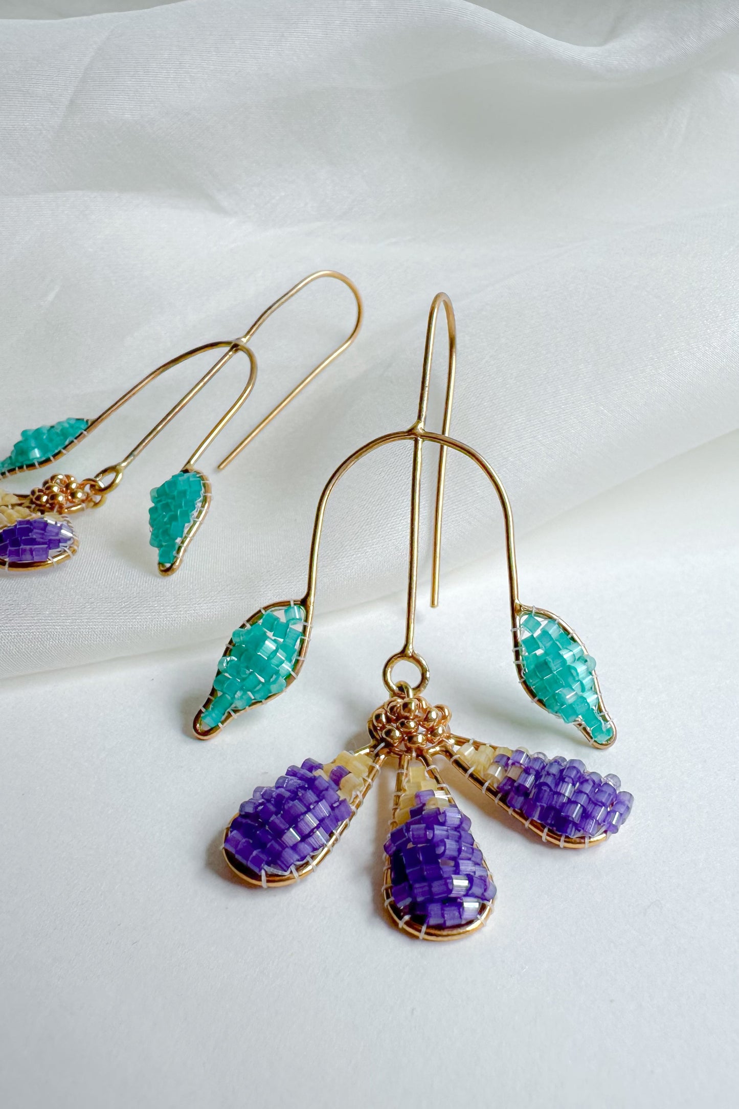 Gold earrings with purple and turquoise gemstones on a white fabric background