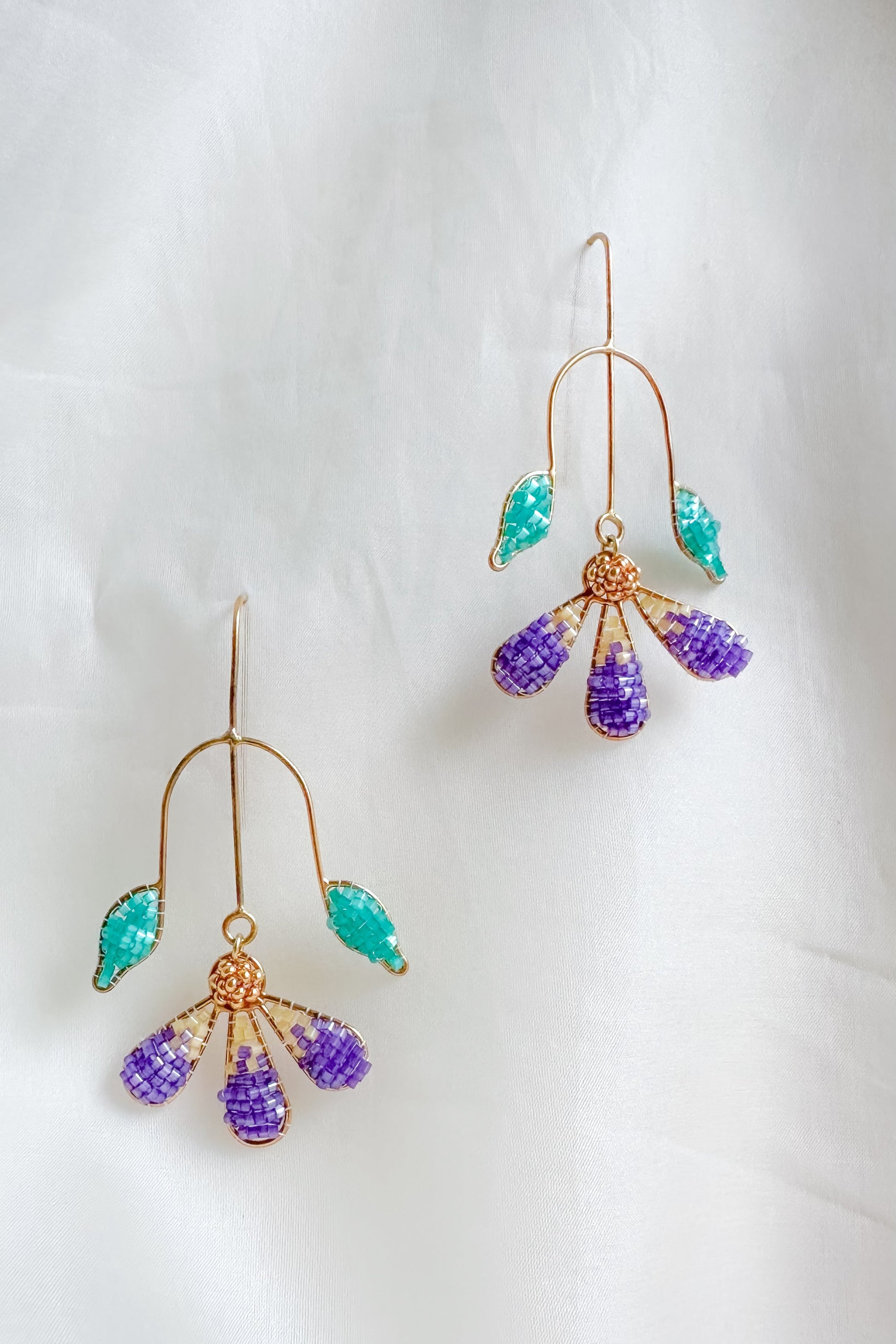 Pair of gold earrings with purple and green beads on a white background