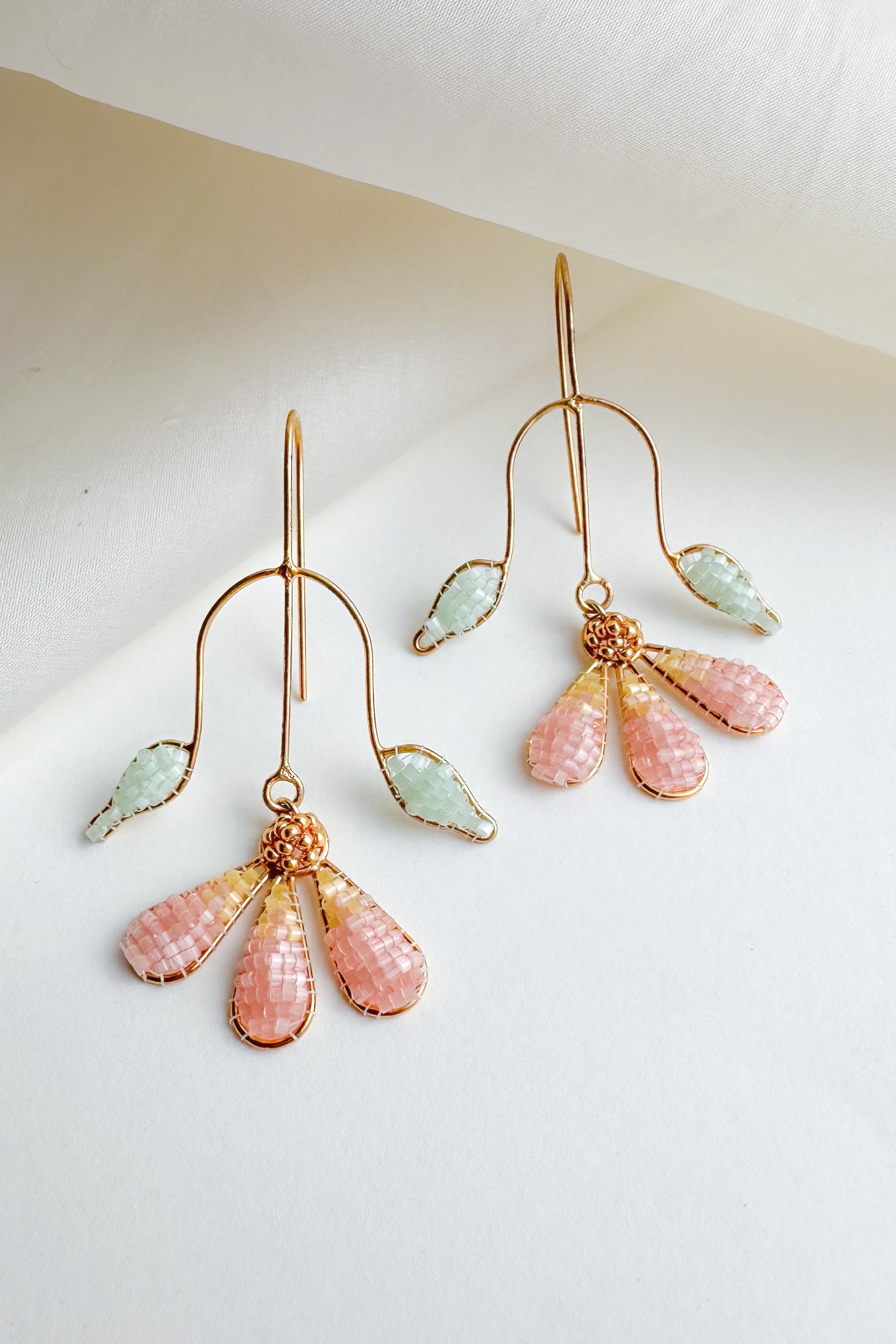 Pair of gold earrings with pink and green gemstones on a white background