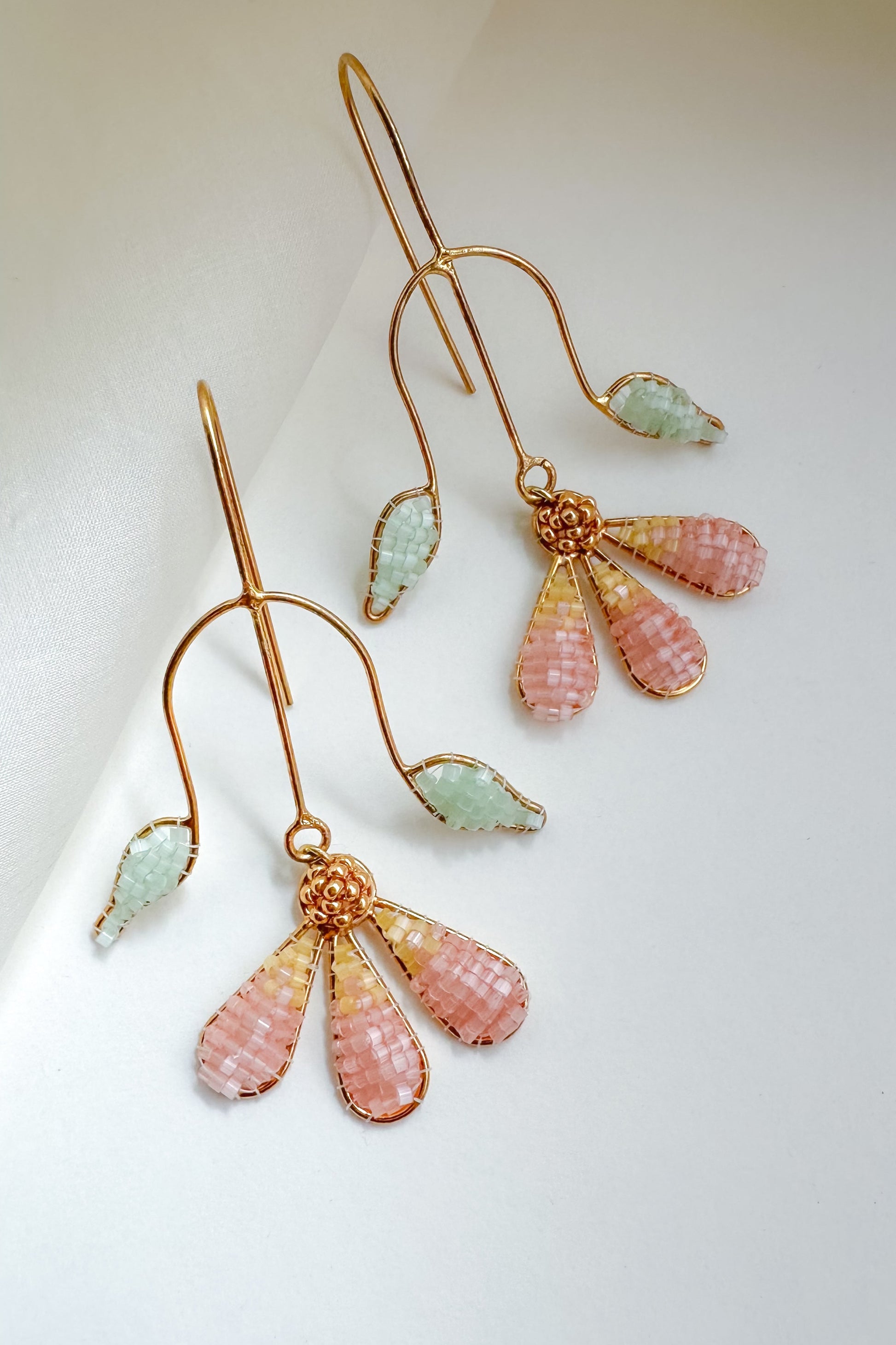Pair of gold earrings with pink and green beads on a white background