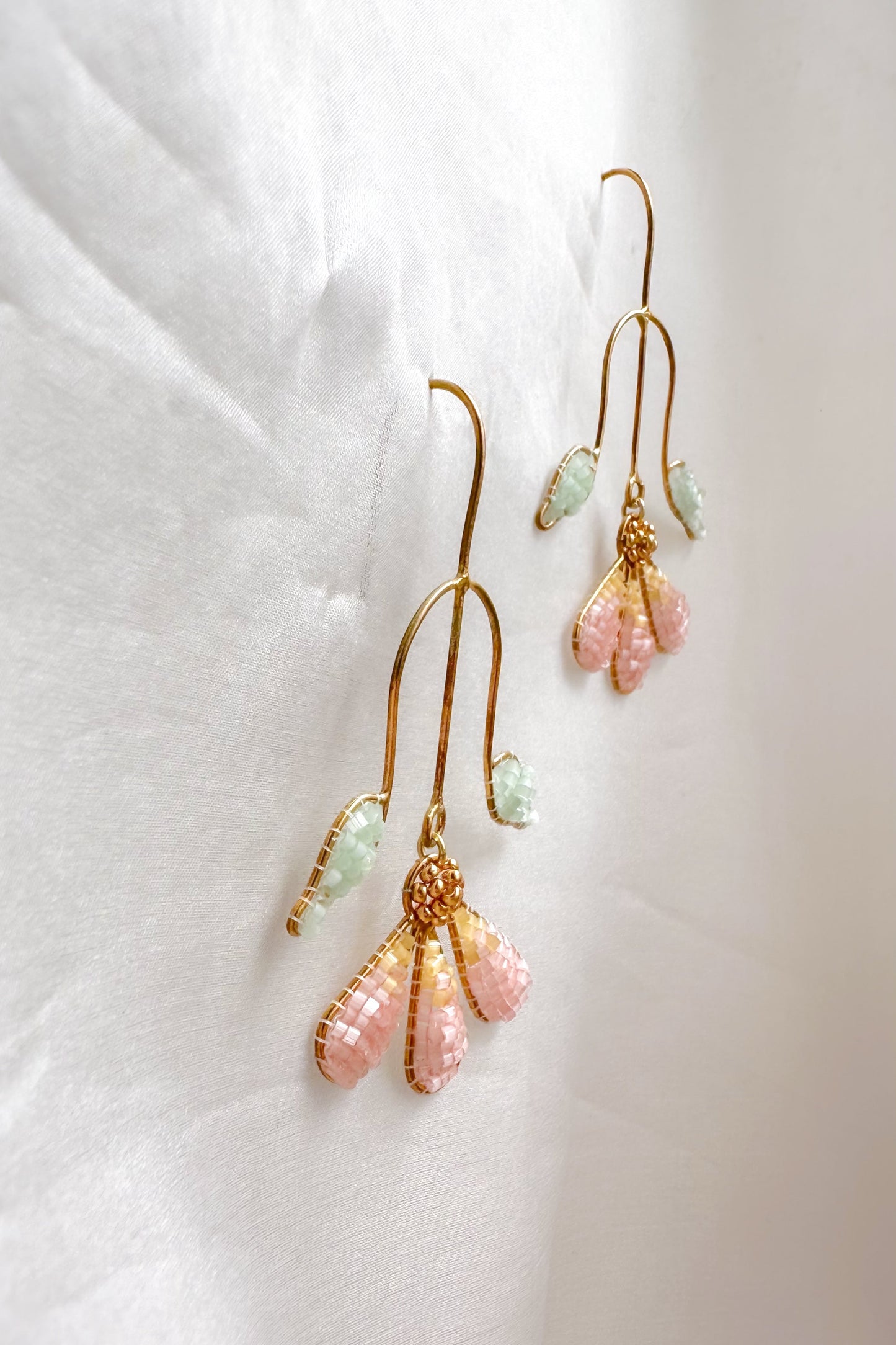 Gold earrings with pink and green beads on a white fabric background