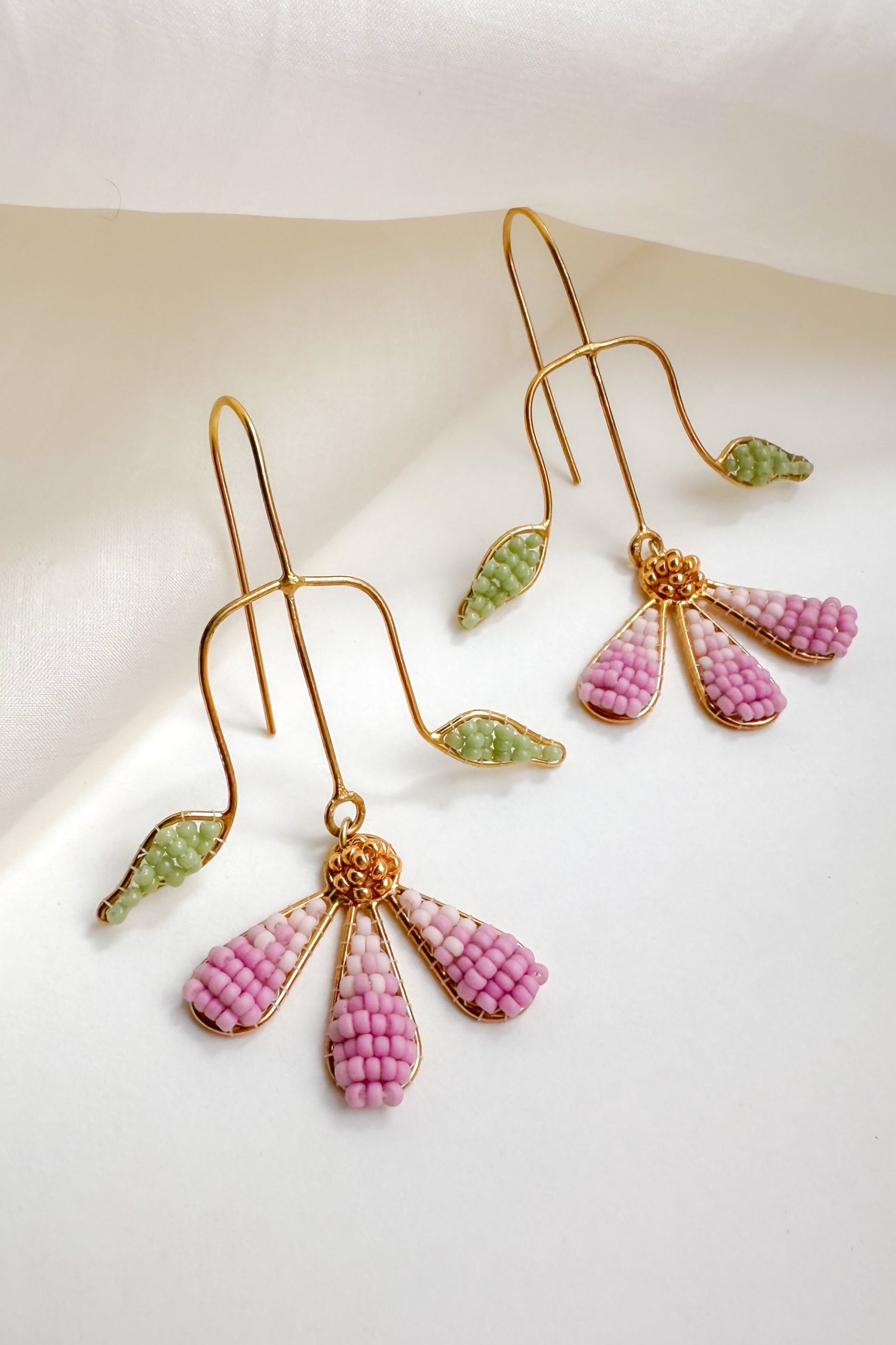 Pair of gold earrings with pink and green beads on a white background