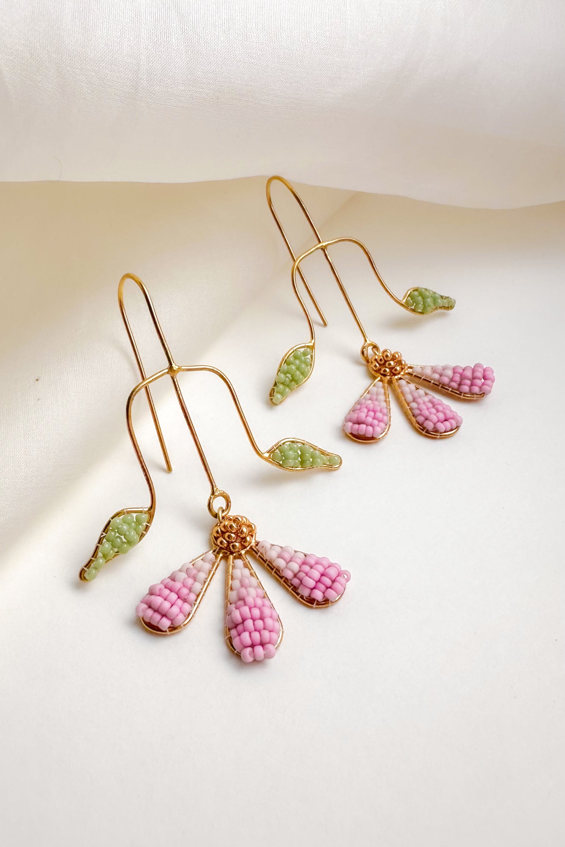 Pair of earrings with pink and green beads on a light background