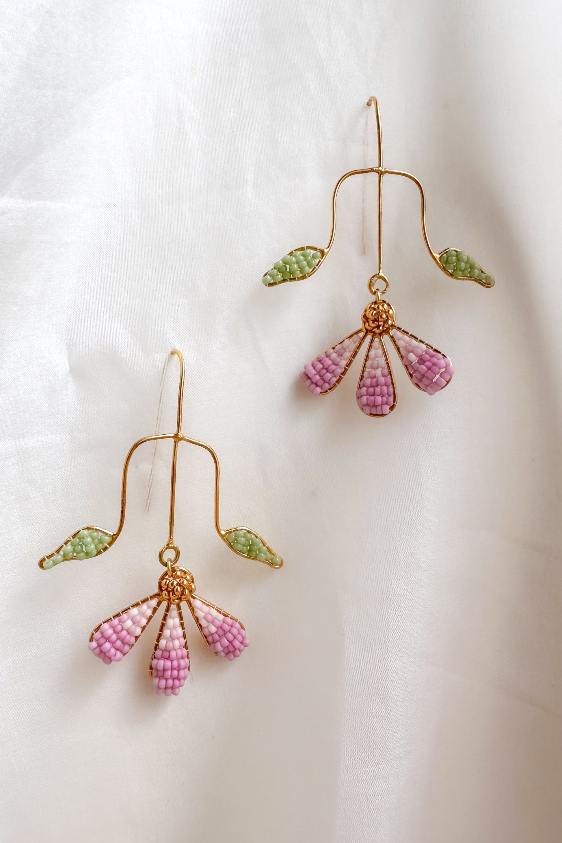 Pair of gold earrings with pink and green beads on a white background