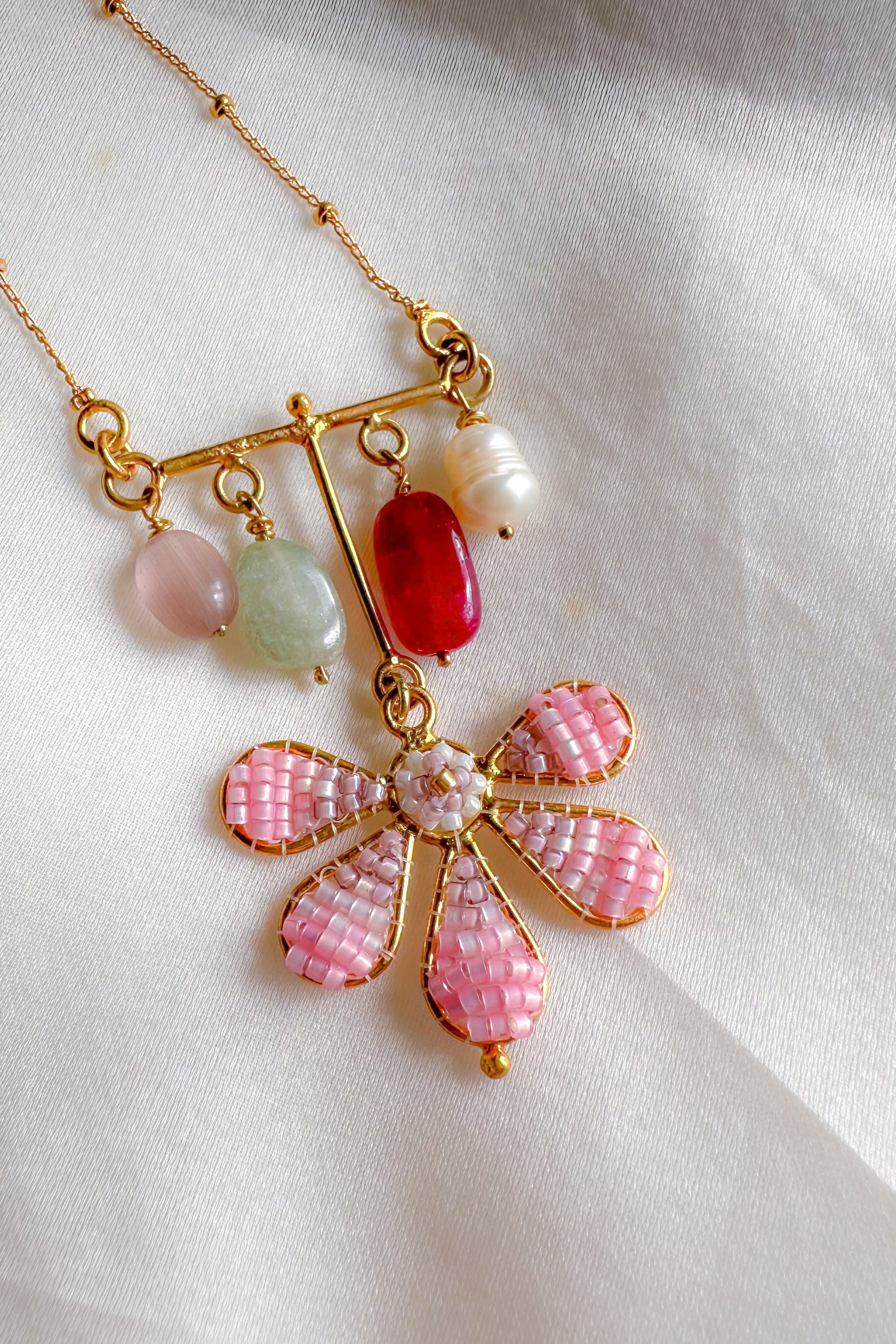 Necklace with a pink floral pendant and colorful beads on a white fabric background
