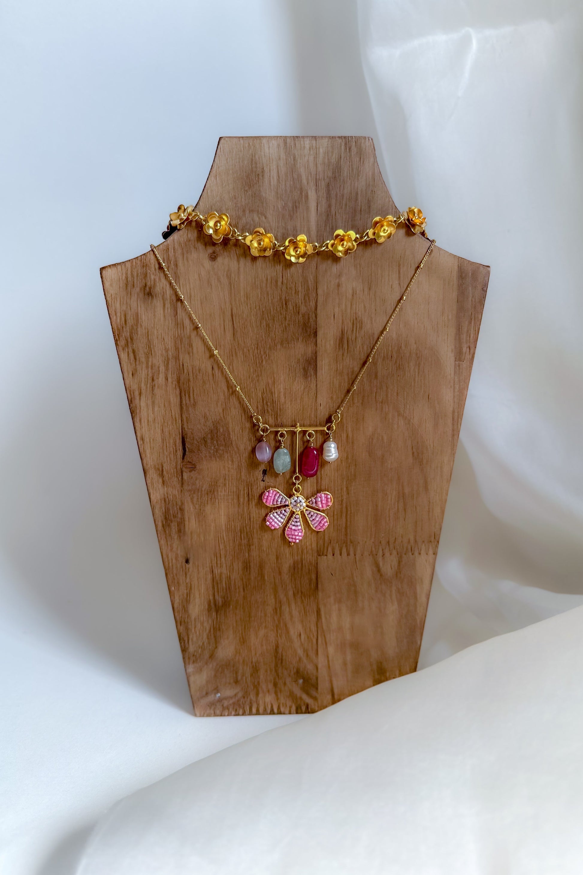 Gold necklace with colorful beads on a wooden mannequin bust against a white background