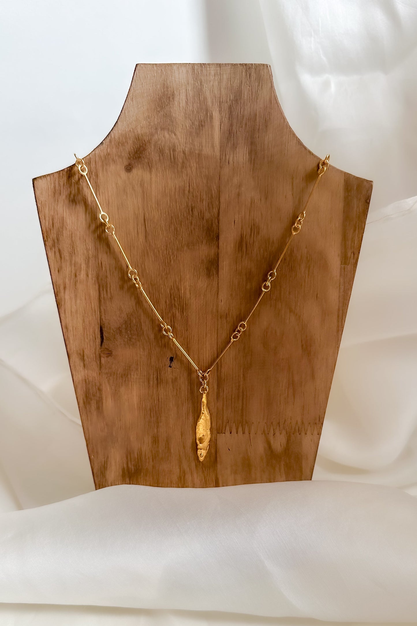 Gold necklace on a wooden mannequin bust against a white background