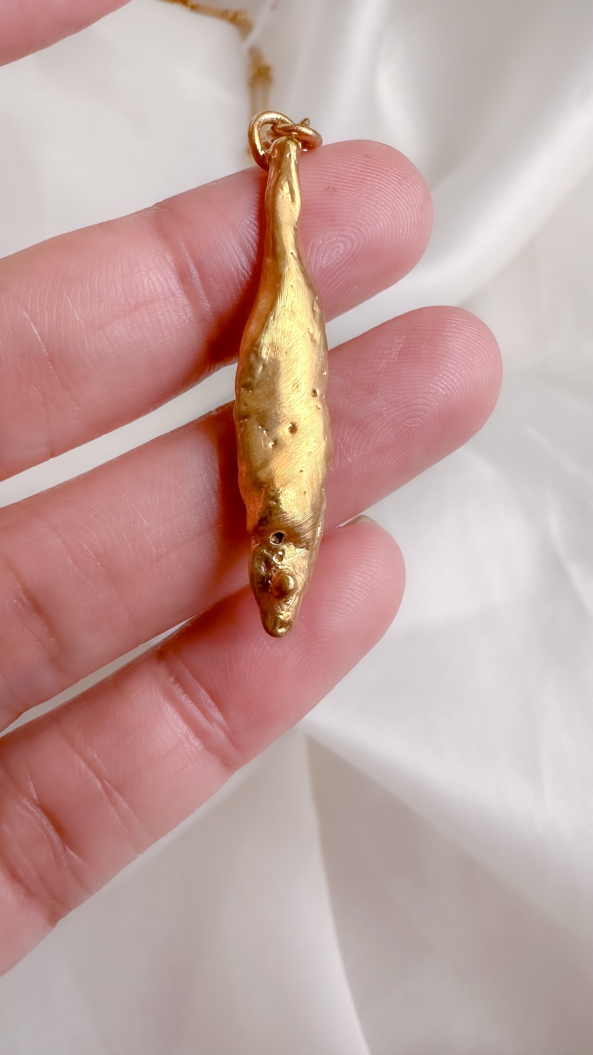 Gold fish-shaped pendant held in a hand against a white background