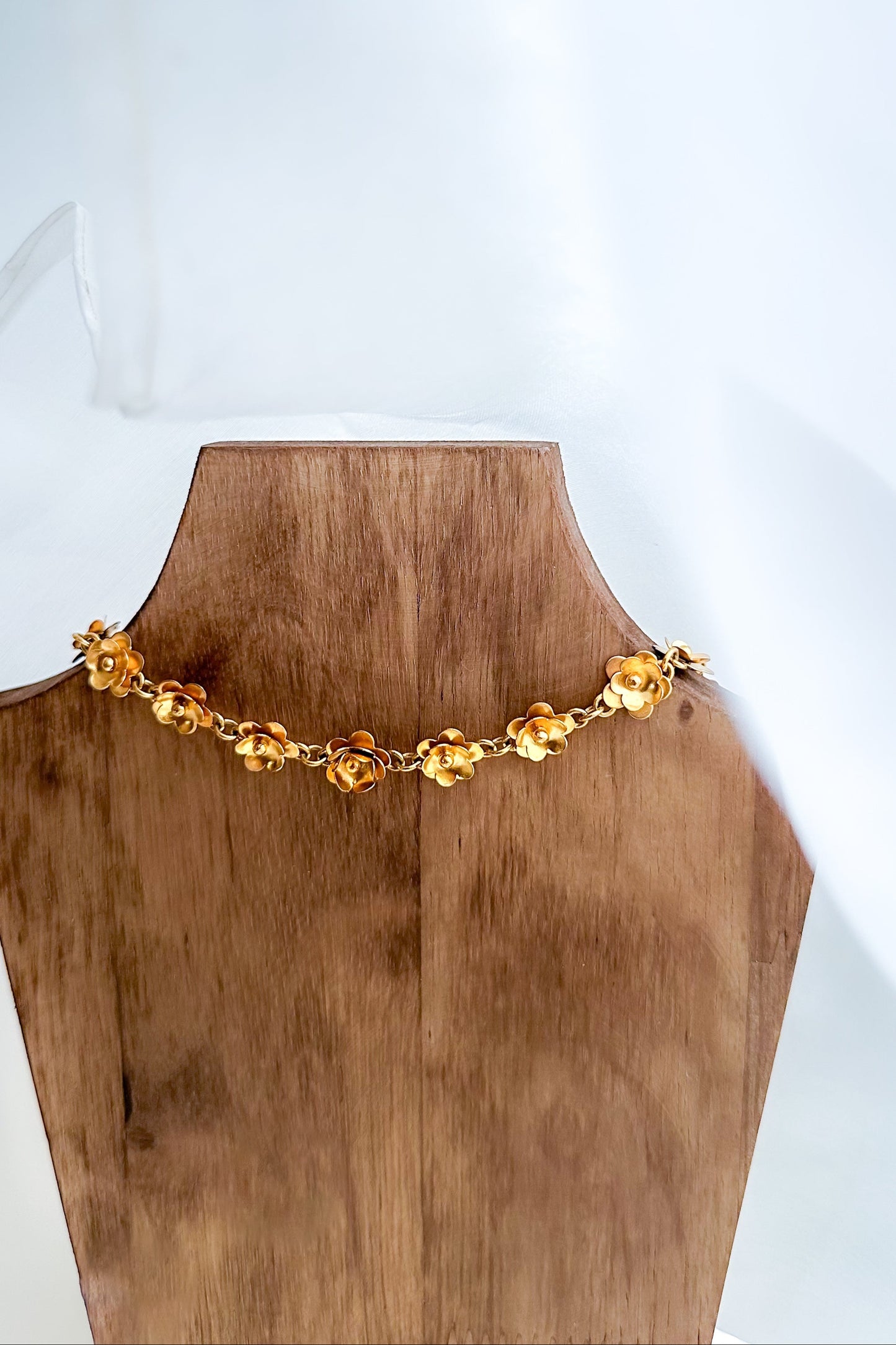 Gold necklace on a wooden mannequin bust against a white background