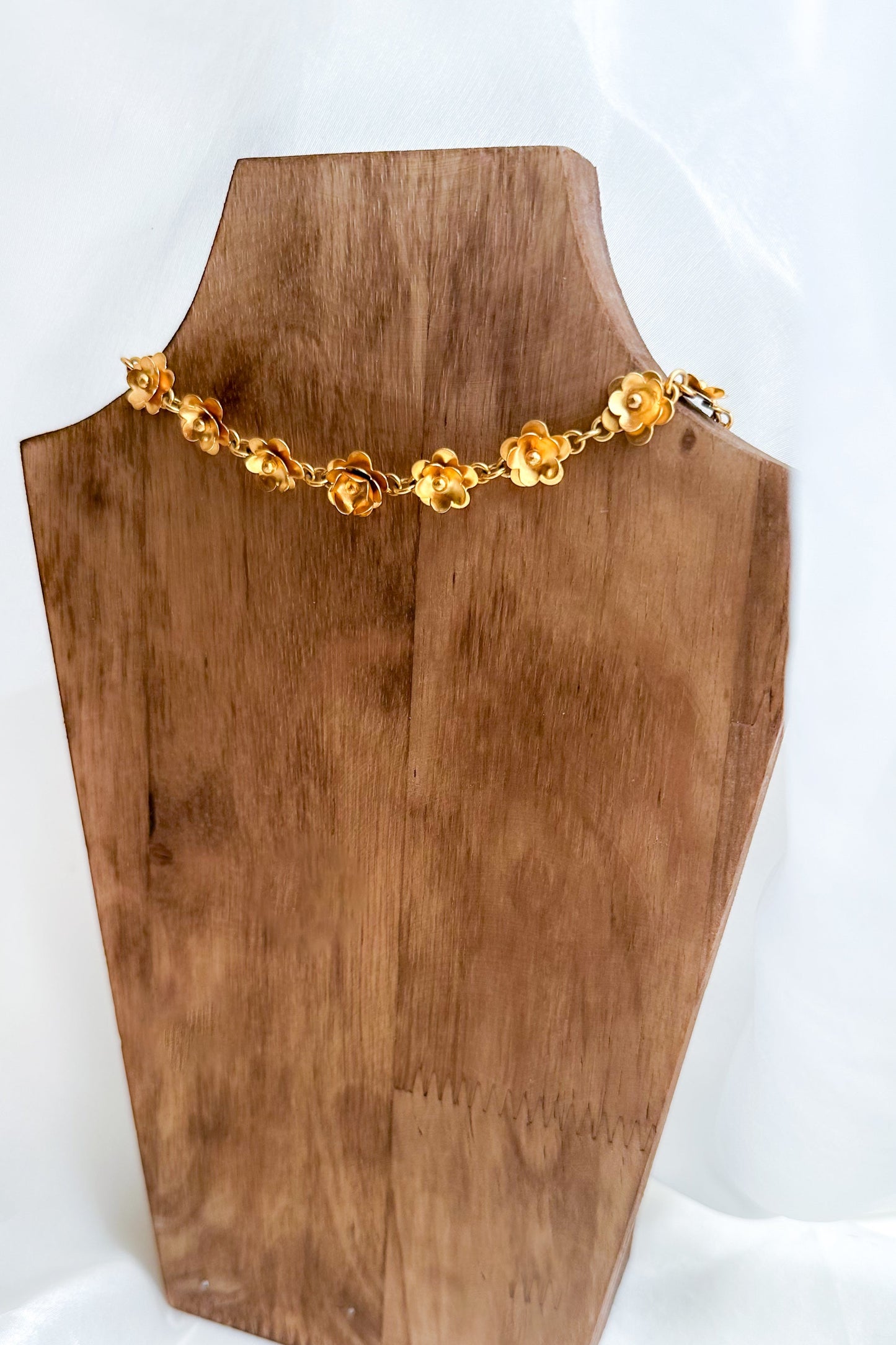 Gold necklace on a wooden mannequin bust against a white background
