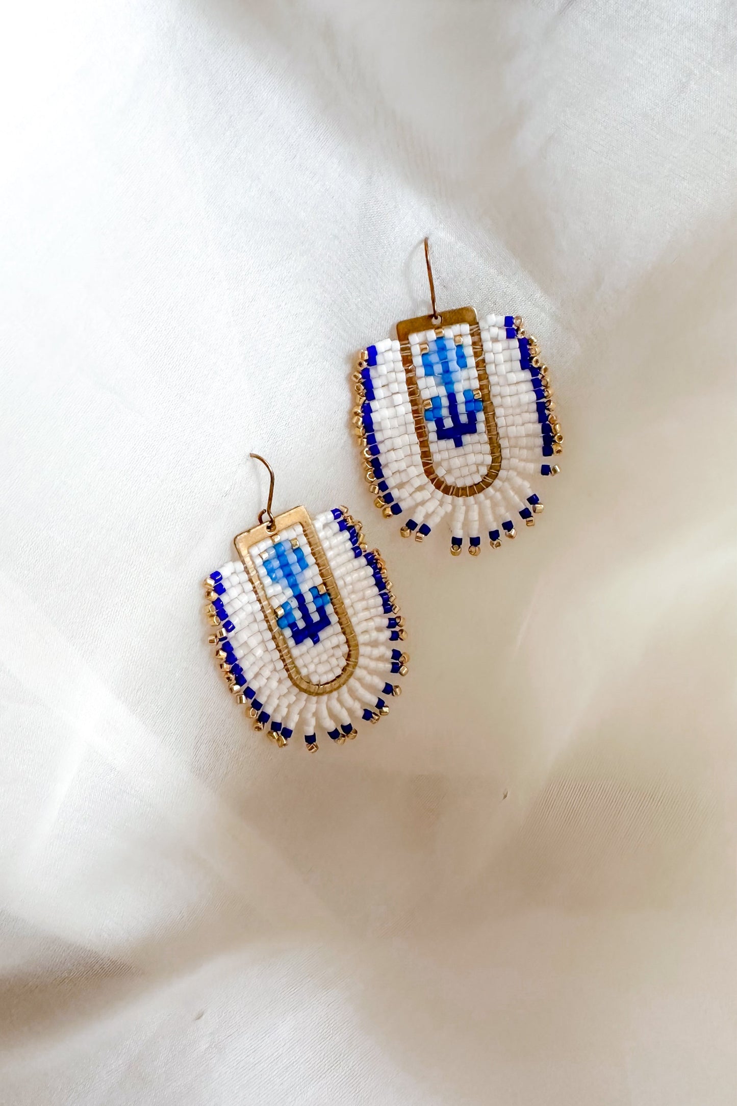 Beaded earrings with blue and gold design on a white fabric background