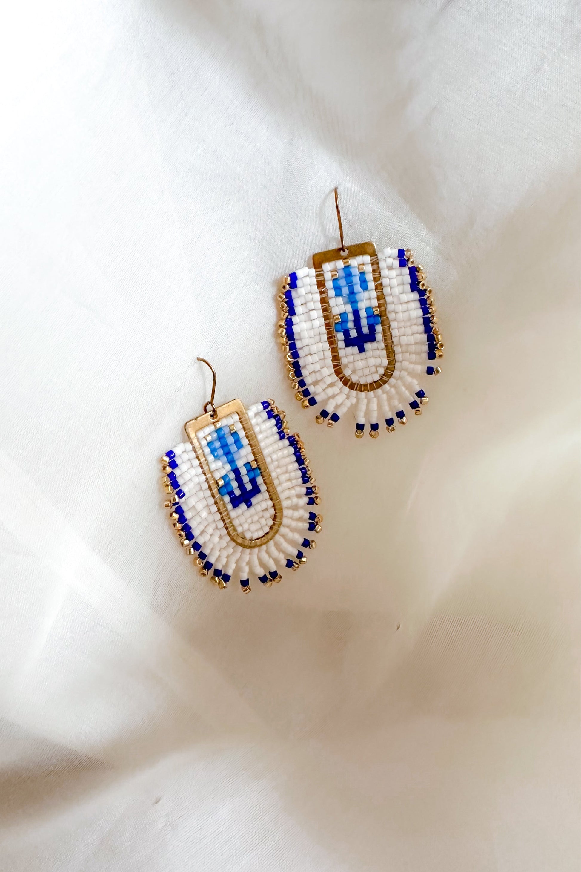 Beaded earrings with blue and gold design on a white fabric background