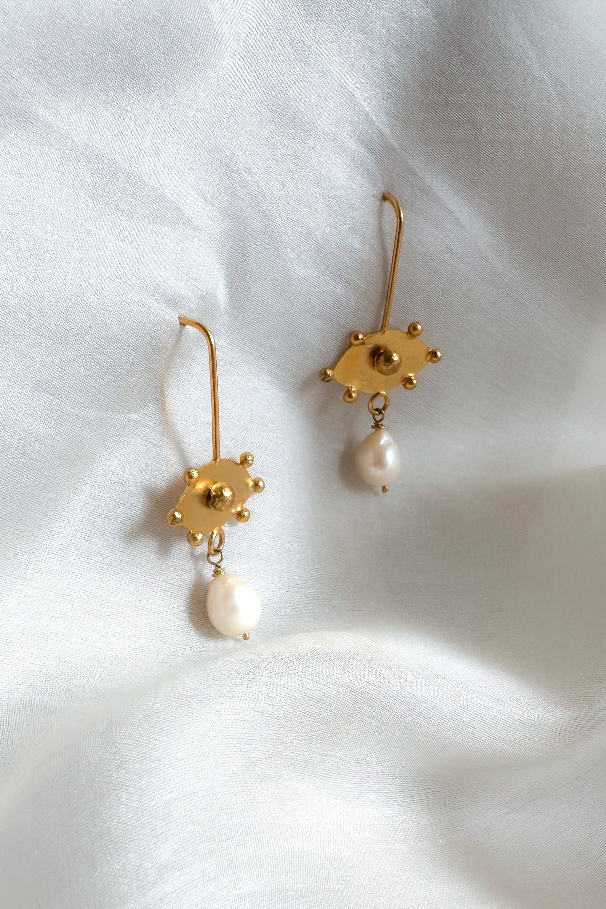 Gold earrings with pearl drops on a white fabric background