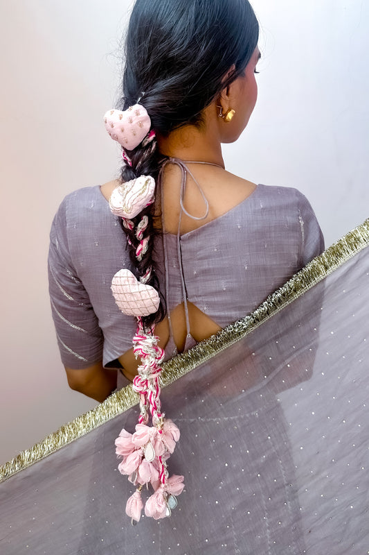 Woman with a decorative braided Parandi wearing a gray saree against a white background