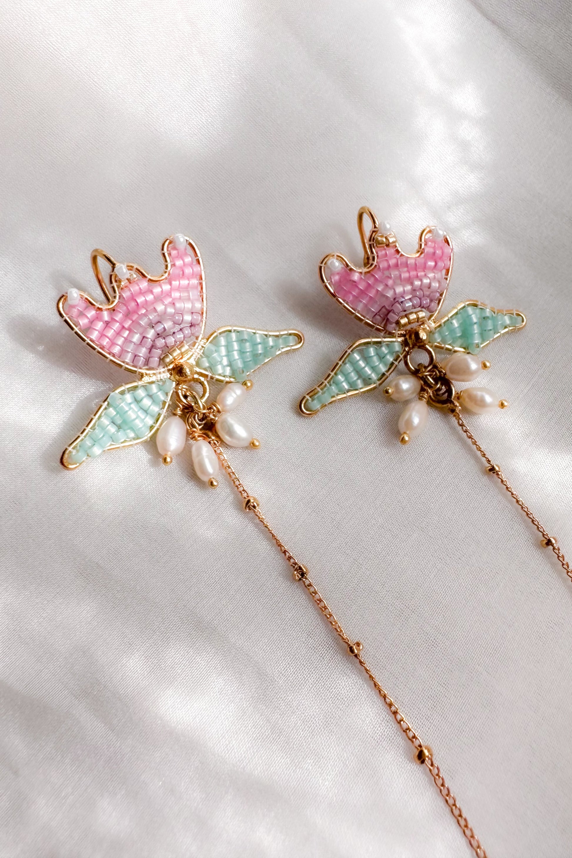 Pair of ear chains with pink and green tulip design on a white background