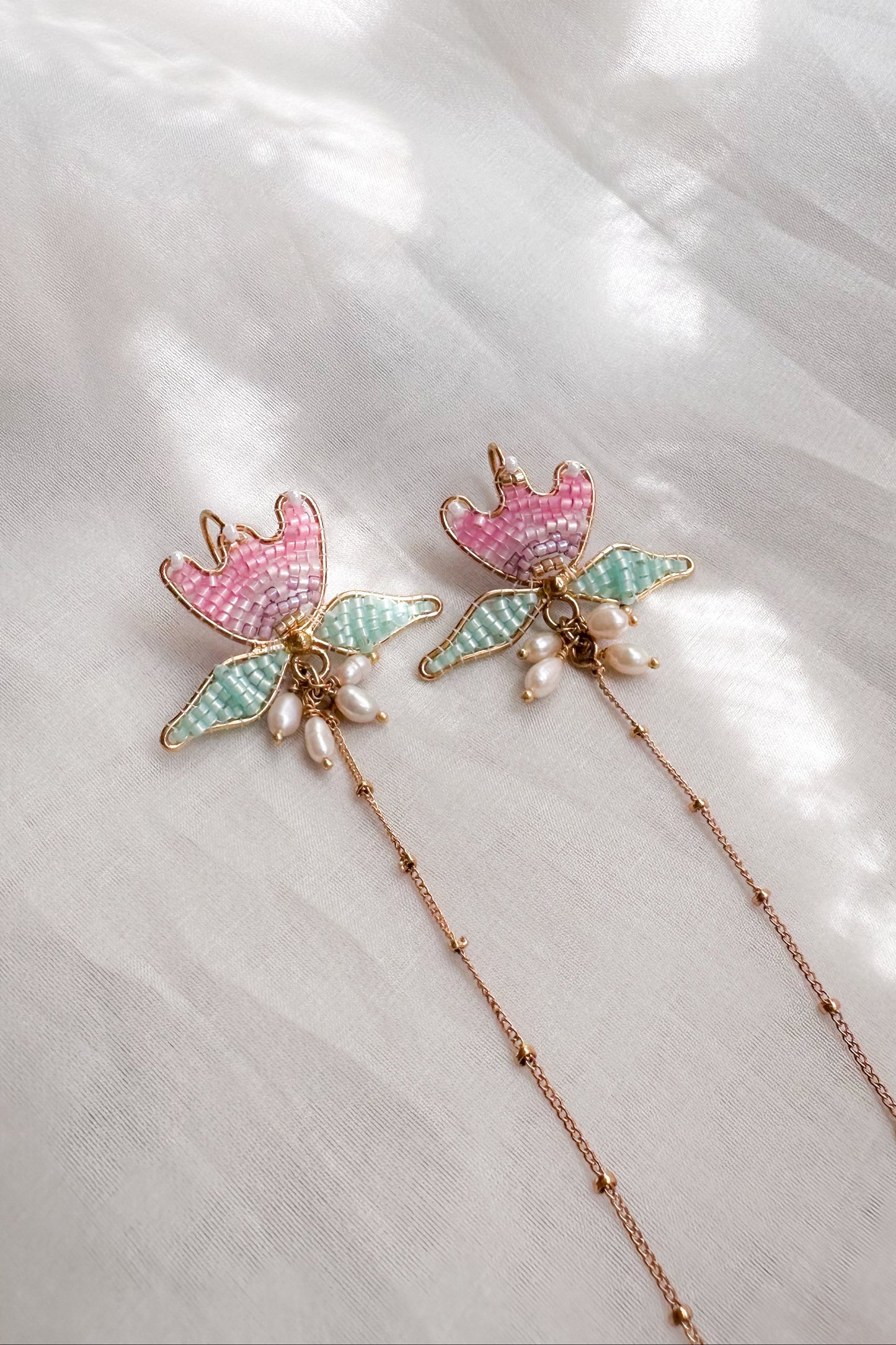 Decorative ear chain with floral designs and pearl accents on a light fabric background