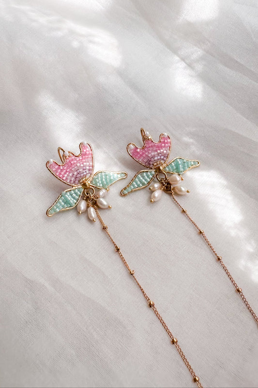 Decorative ear chain with floral designs and pearl accents on a light fabric background