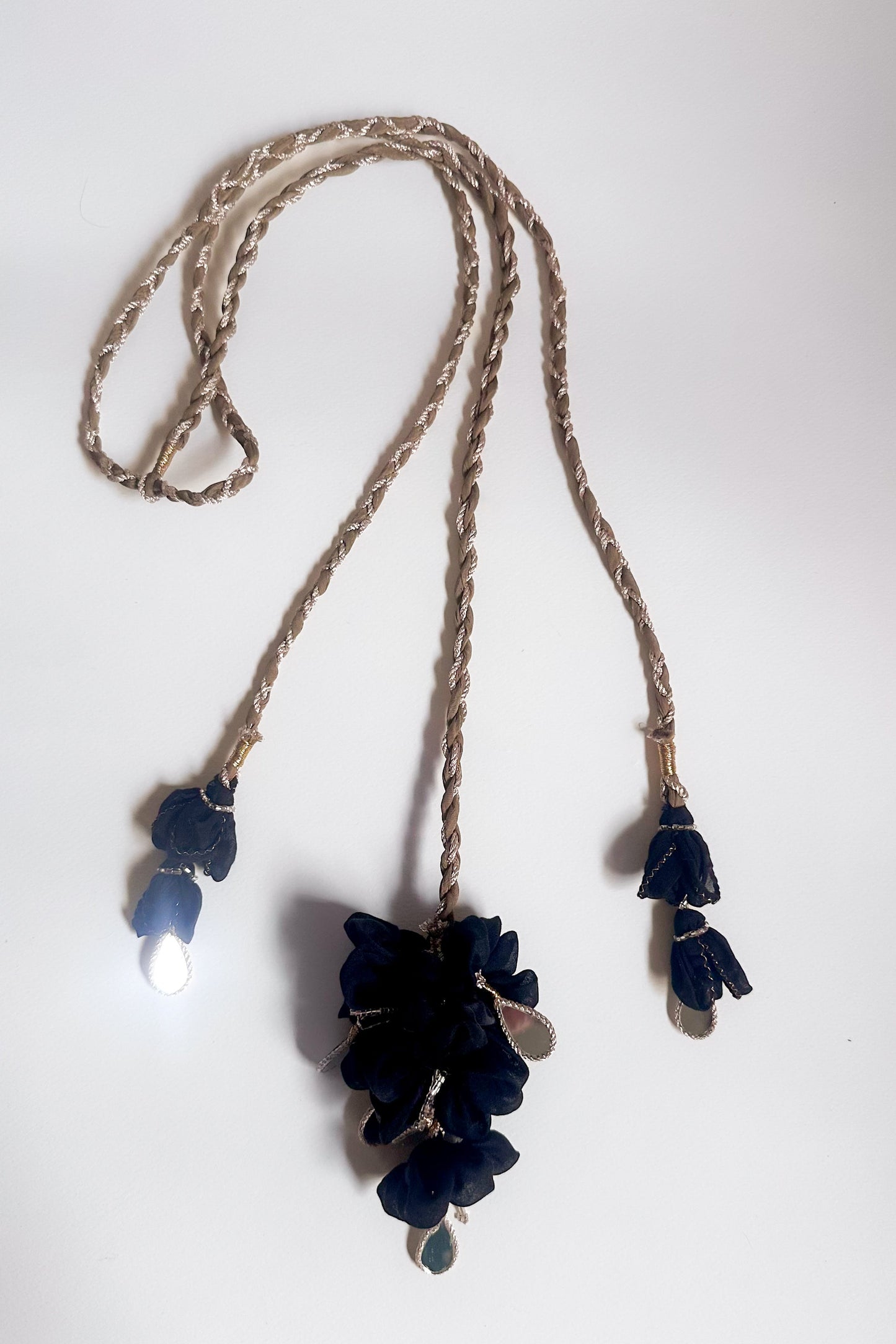 Parandi with black floral pendants on a Olive gold  braided cord against a white background