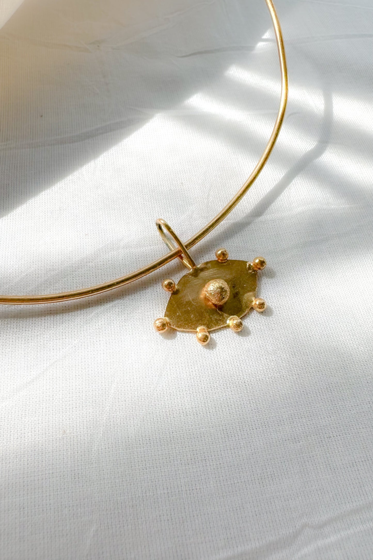 Gold choker necklace with evil eye pendant on a white fabric background