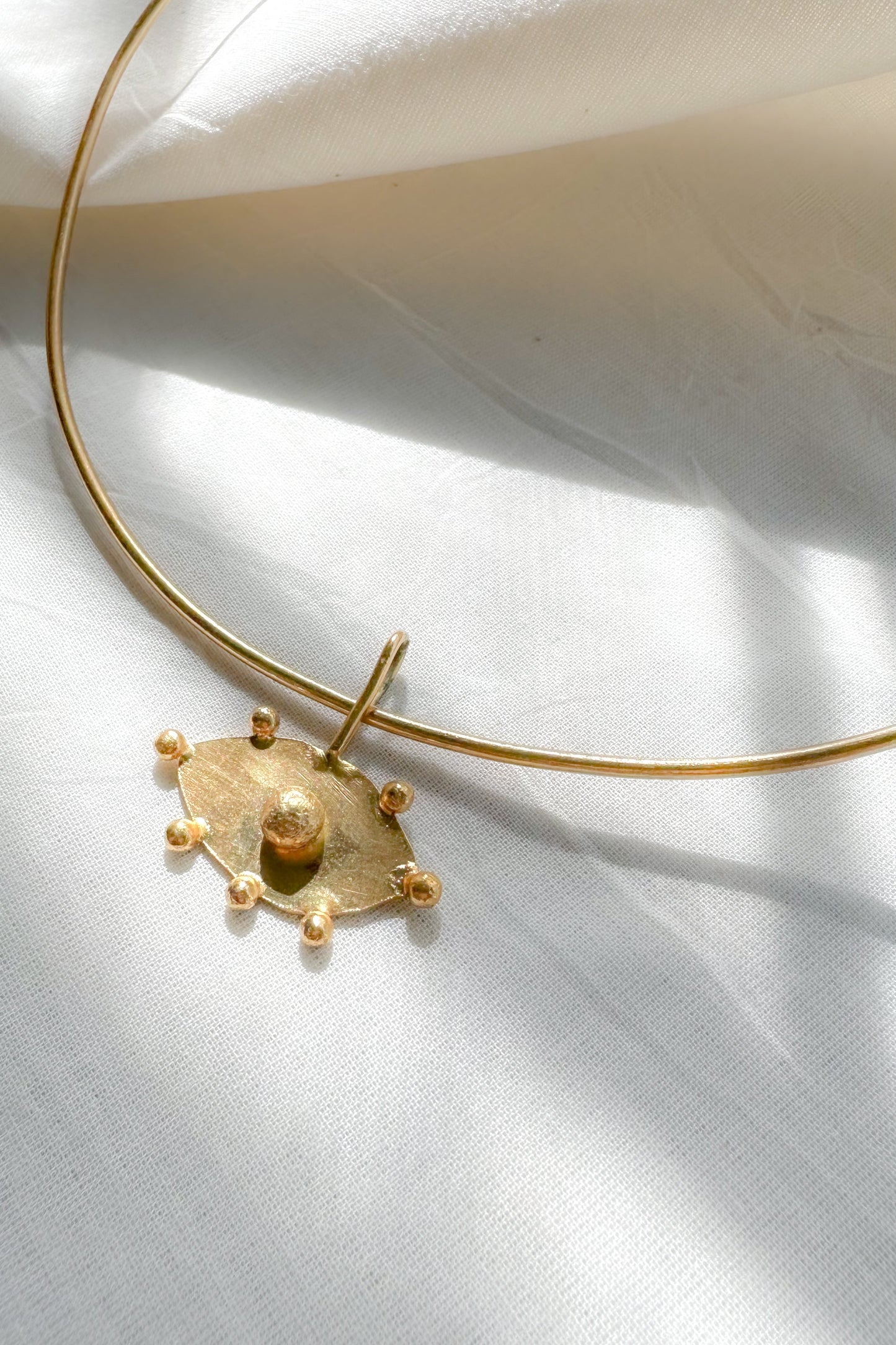 Gold choker necklace with evil eye pendant on a white fabric background